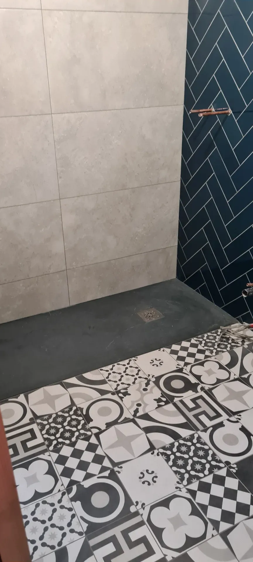 Slate-effect shower tray beside patterned floor tiles and blue herringbone walls