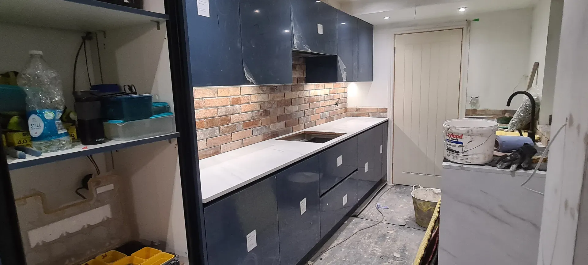Newly fitted navy kitchen with a brick-effect splashback, protective film still on