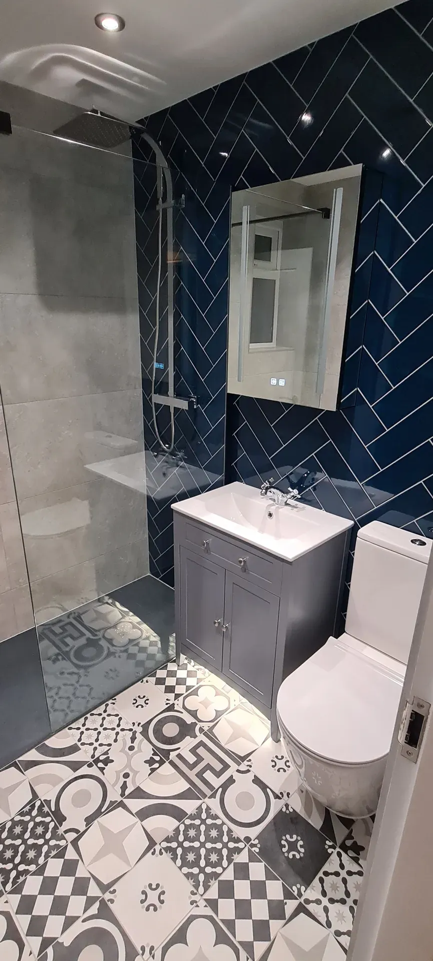 Vanity unit and toilet against navy herringbone tiling with a patterned floor