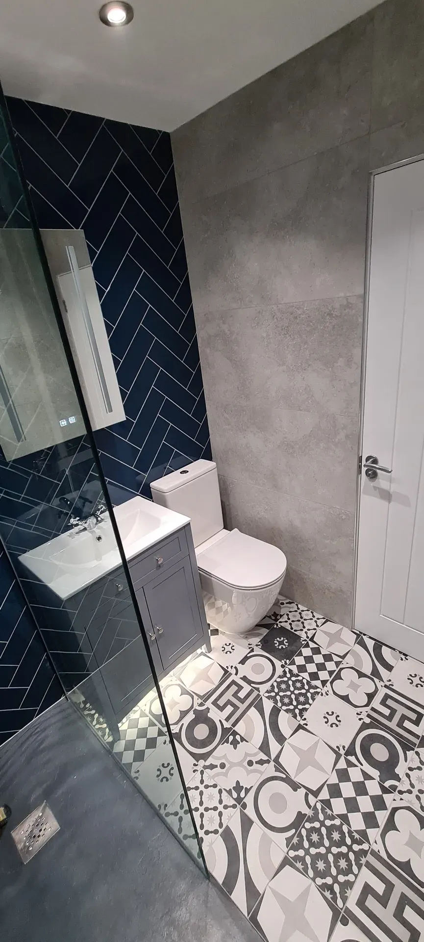 Grey vanity unit and toilet against navy herringbone tiles and a patterned floor