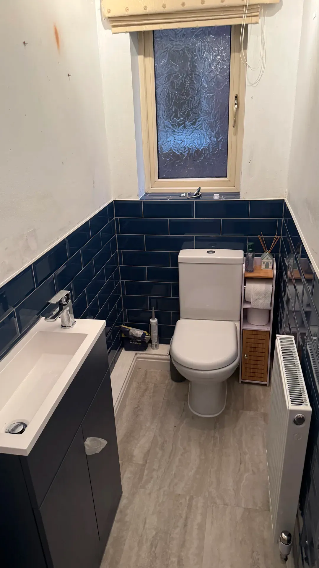 Close-coupled toilet and vanity basin against dark blue metro tiling