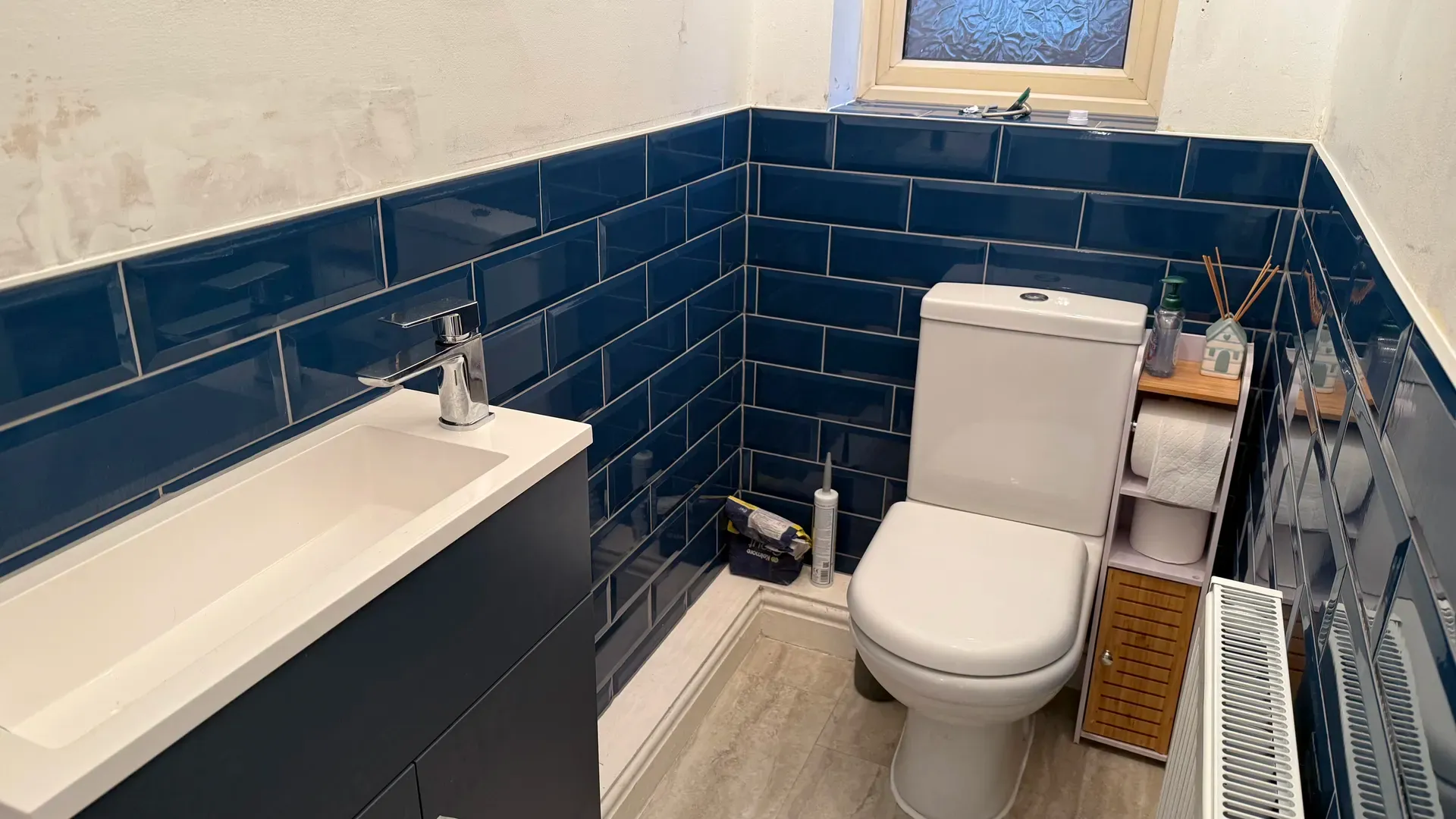 Vanity unit and toilet against dark blue metro tiling