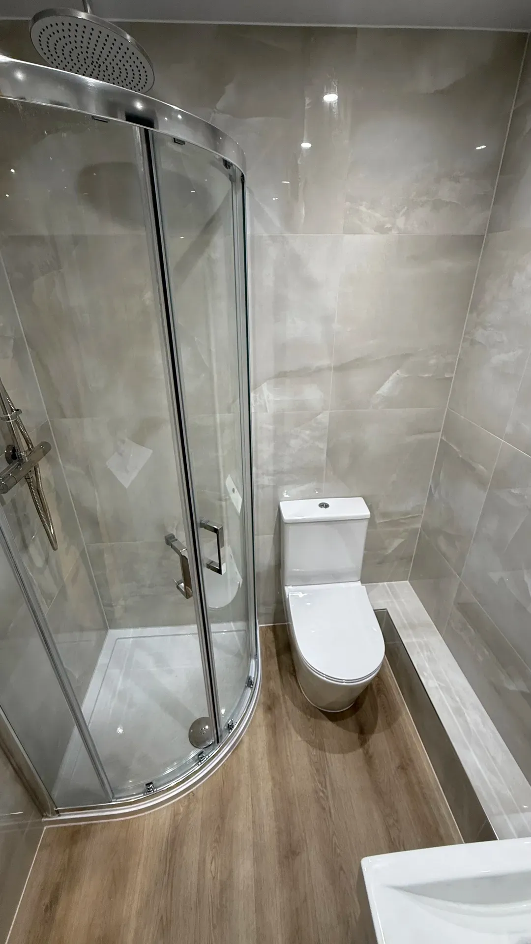 Quadrant shower enclosure beside a close-coupled toilet on marble-effect tiling