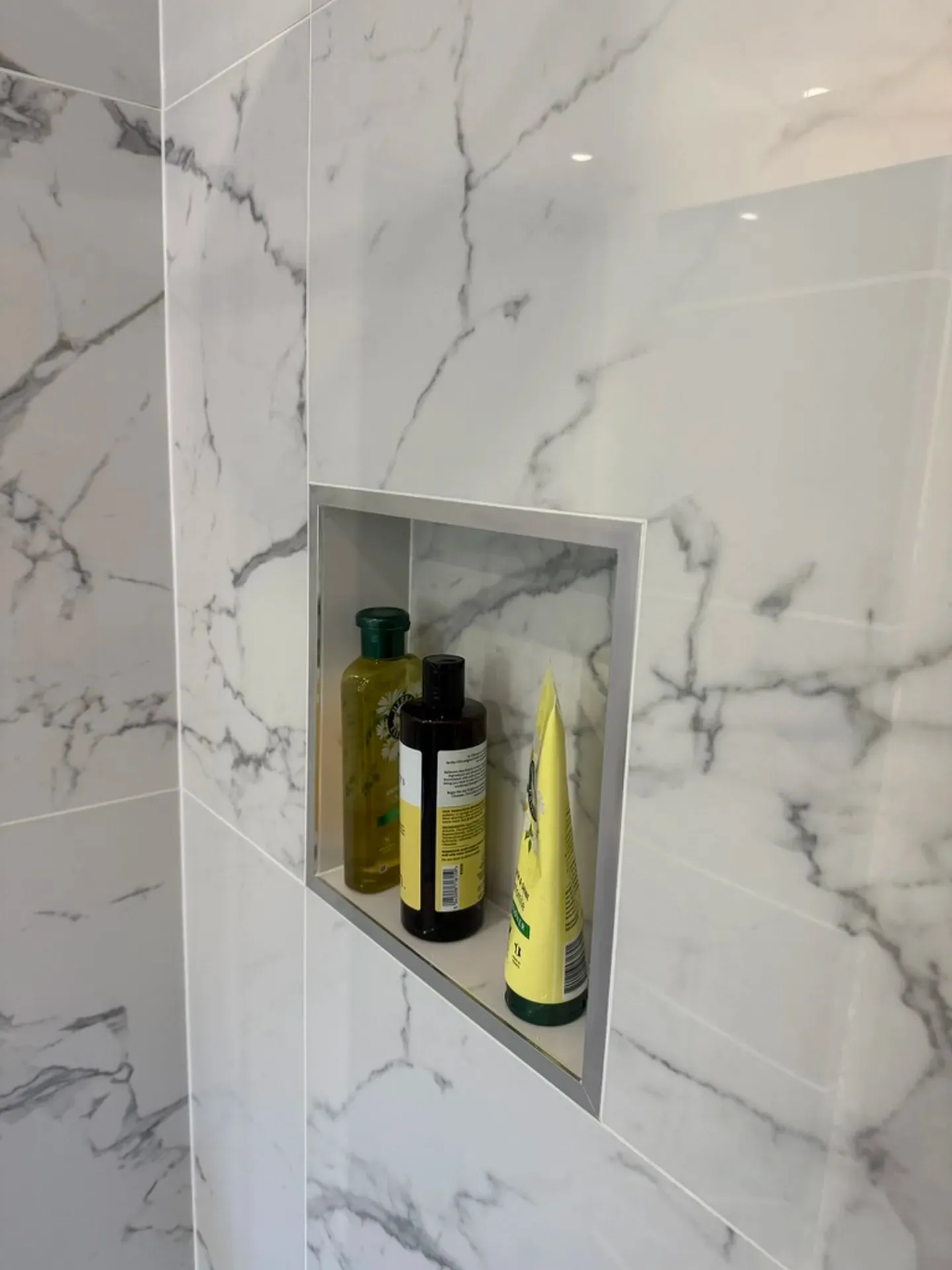 Recessed tiled shelf set into a marble-effect shower wall