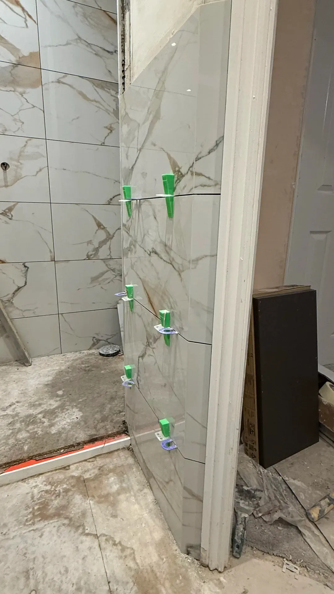 Marble-effect tiles going up on a stripped wall with levelling clips fitted