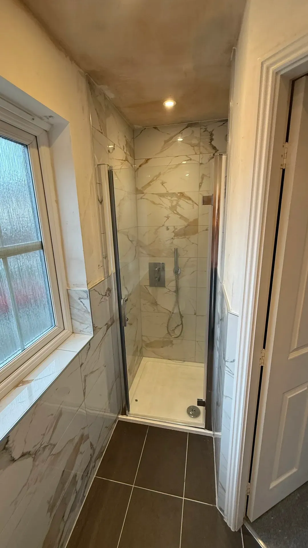 Shower enclosure beside an obscure-glazed window with warm marble-effect tiling