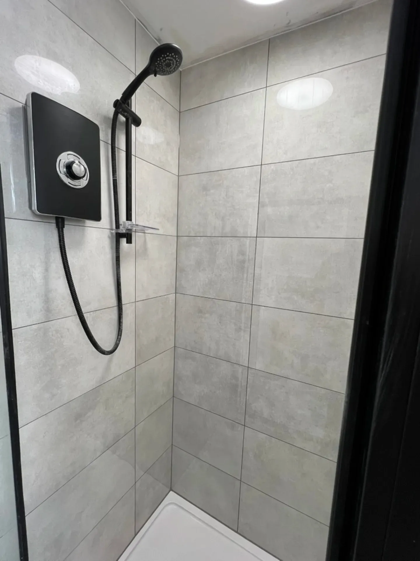 Black shower valve and riser rail on large-format grey tiling