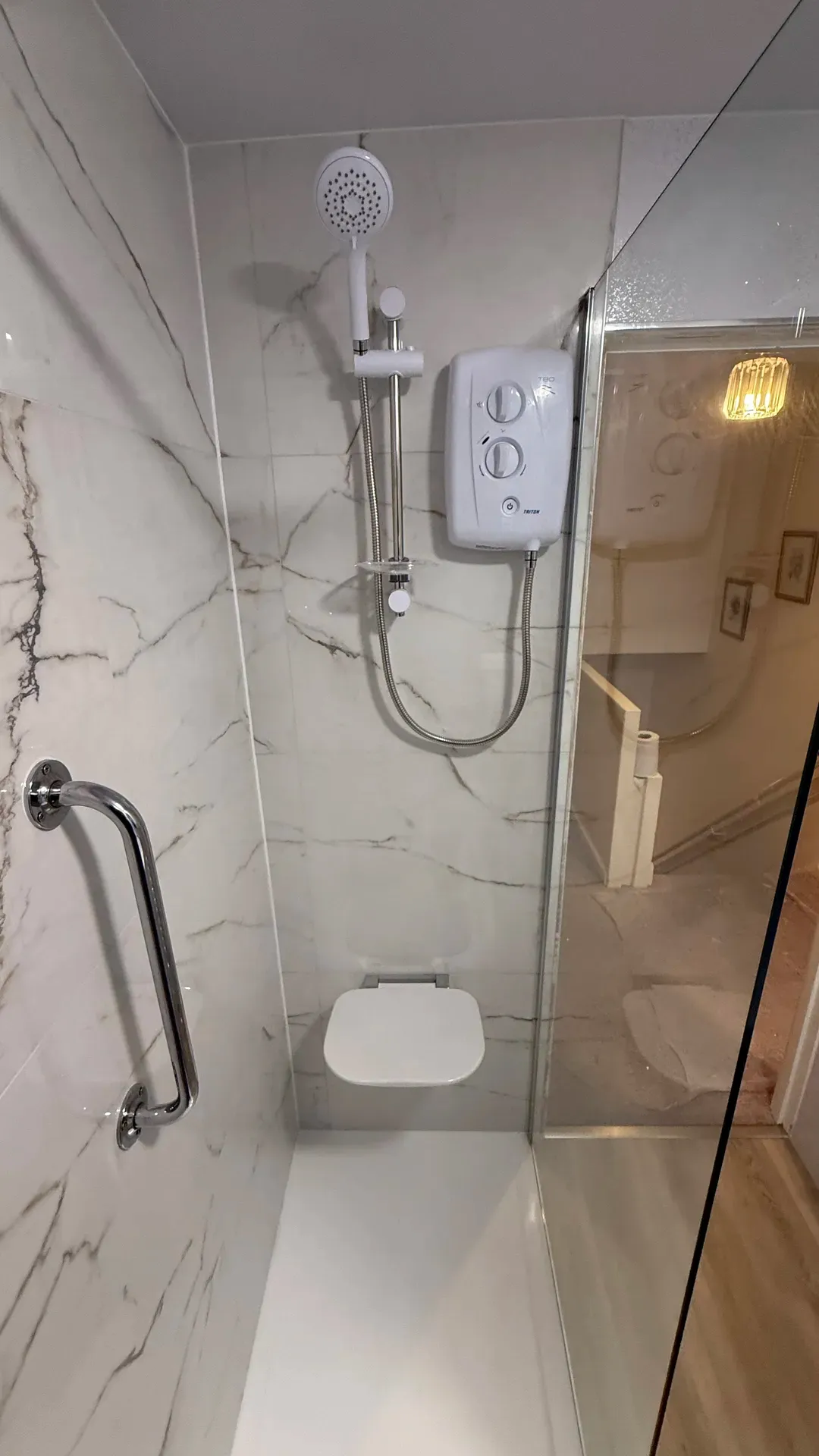 Electric shower with a grab rail and fold-down seat in an accessible shower enclosure
