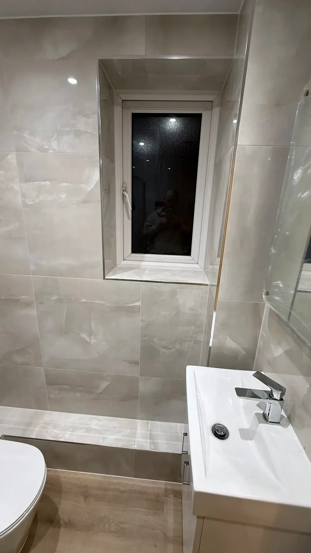 Marble-effect tiled bathroom with a narrow window and a black basin tap