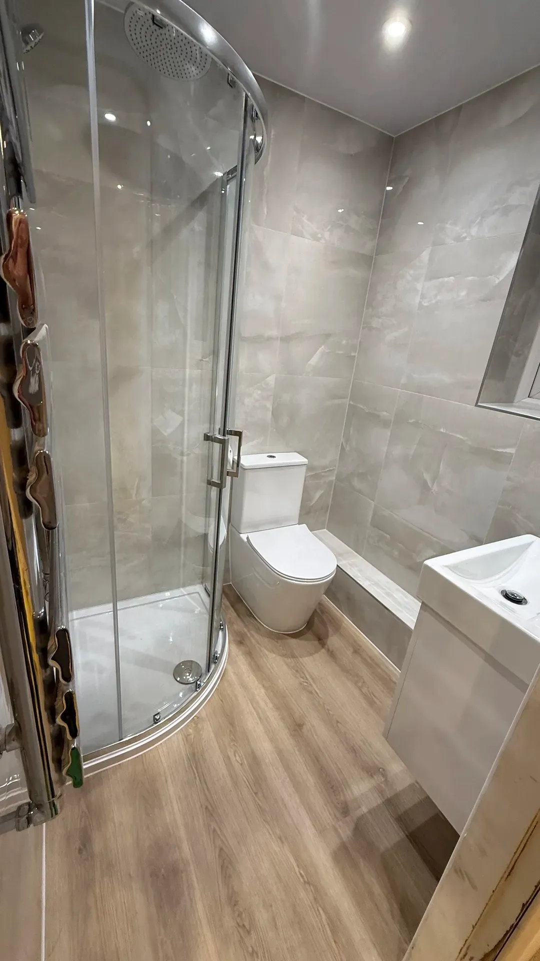 Quadrant shower enclosure, toilet and basin in a grey-tiled bathroom