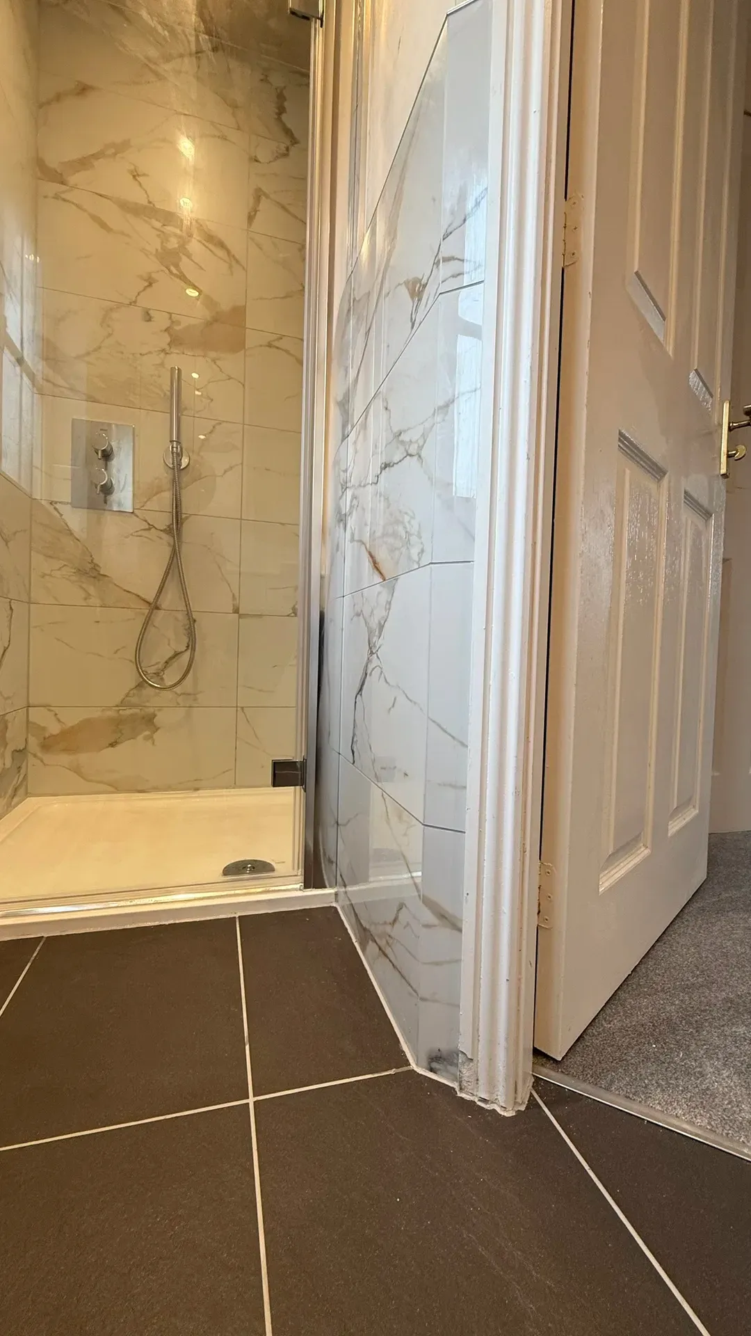 Shower tray and warm marble-effect tiling beside a panelled door