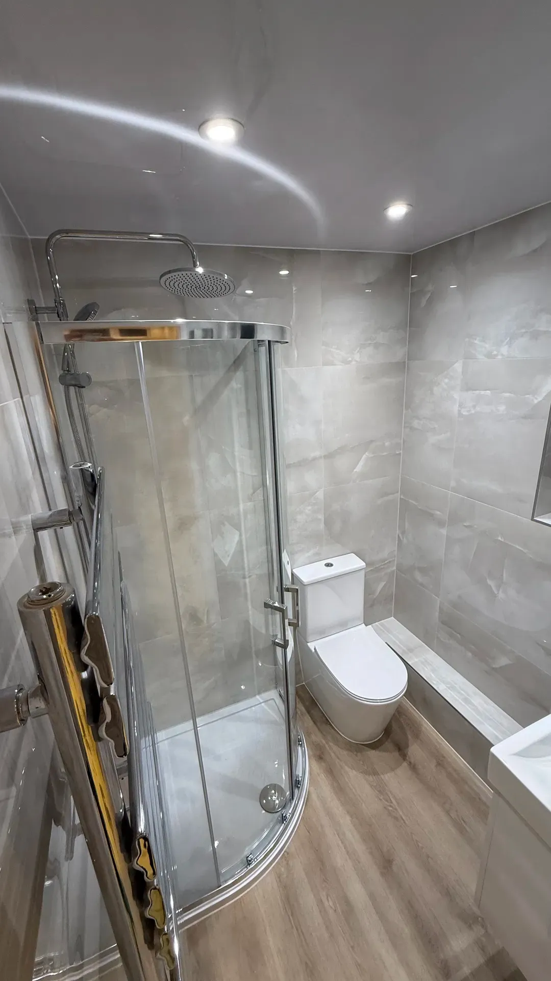 Quadrant shower enclosure and toilet in a grey-tiled bathroom