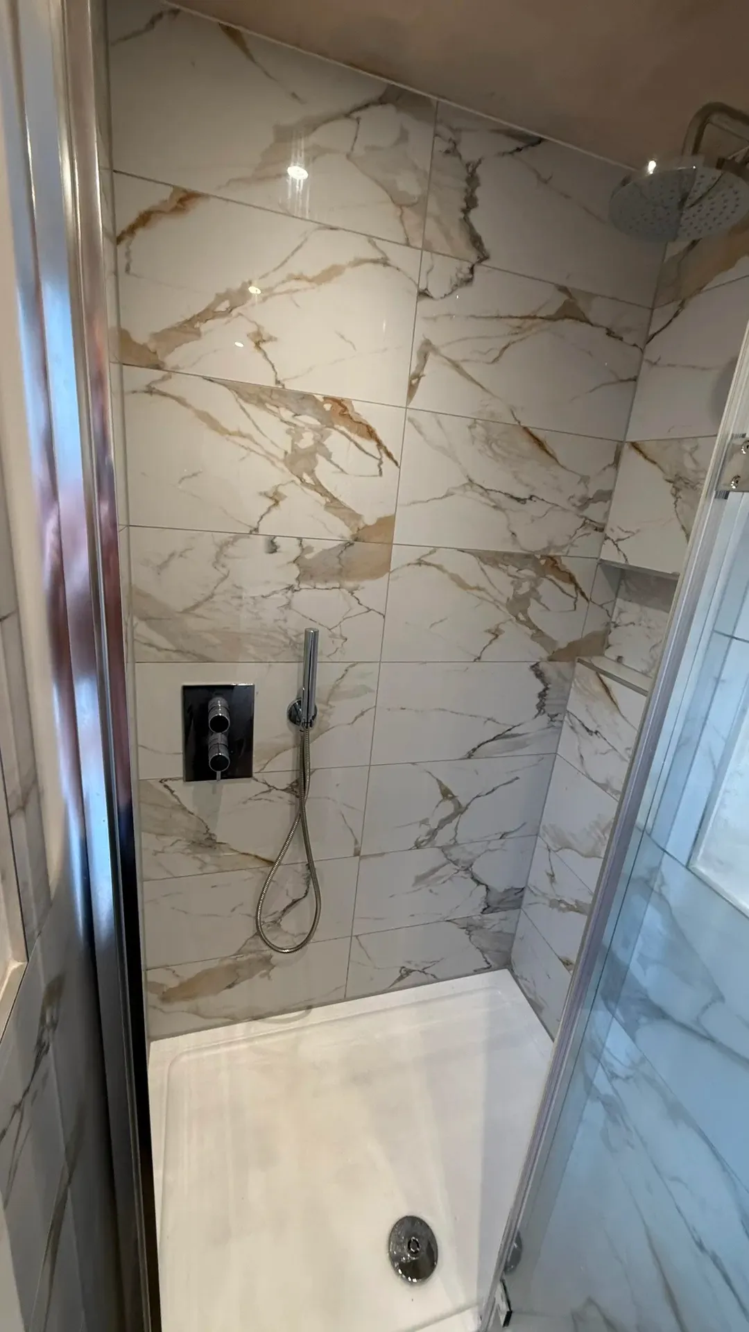 Concealed shower valve and riser on veined marble-effect tiling