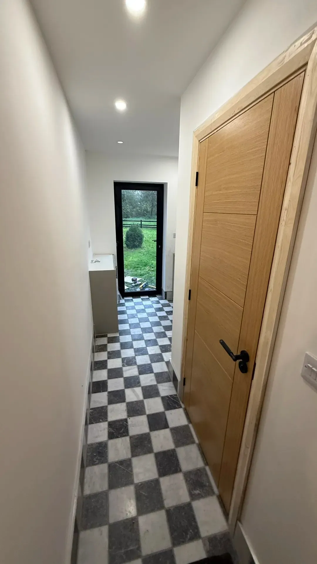 Newly plastered landing with an oak door and a chequerboard tiled floor