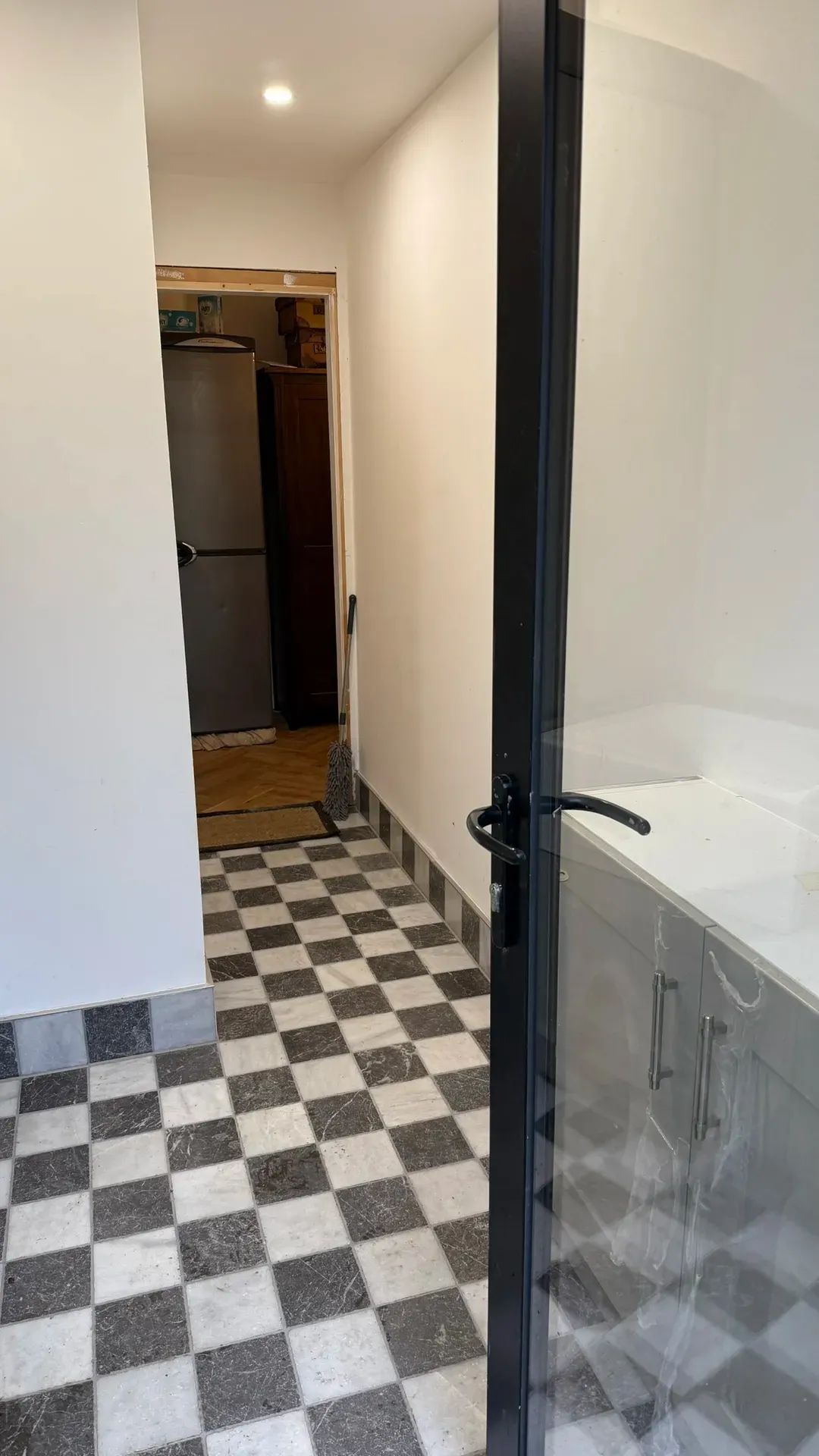 Bath and fitted units seen from a hallway with a chequerboard tiled floor