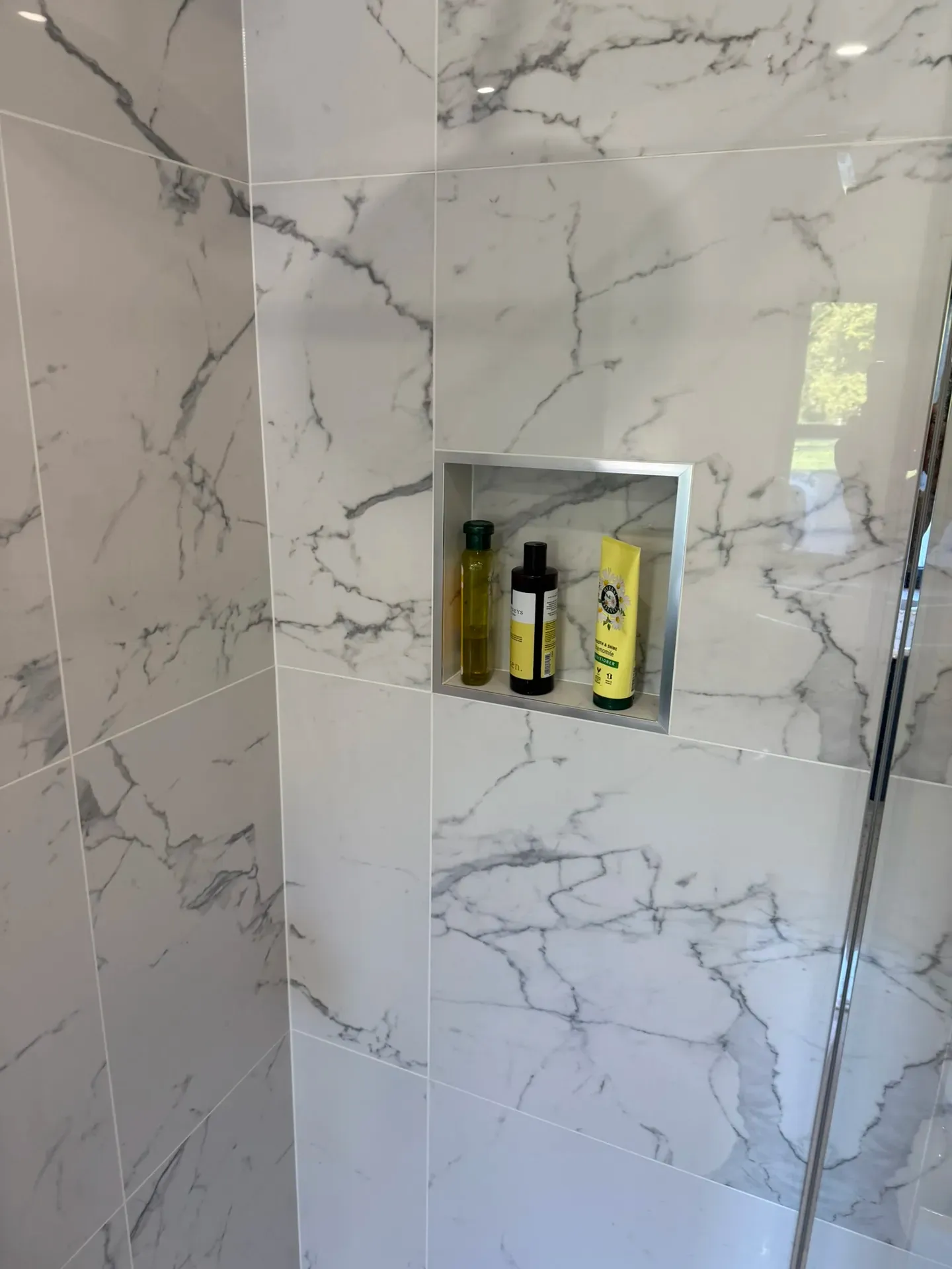 Walk-in shower with a glass screen and a recessed shelf in marble-effect tiling