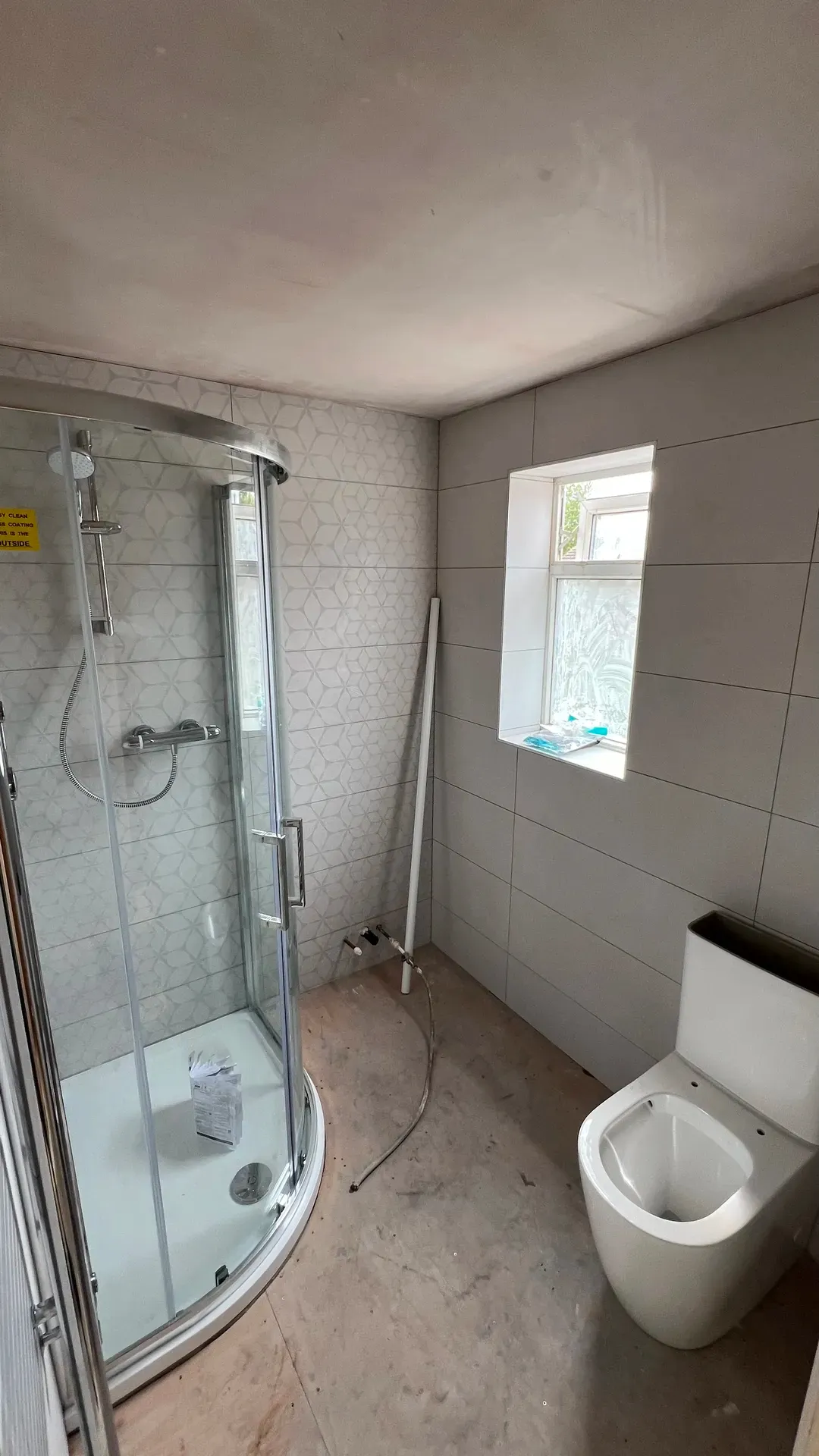 Quadrant shower enclosure and toilet in a tiled shower room with a window