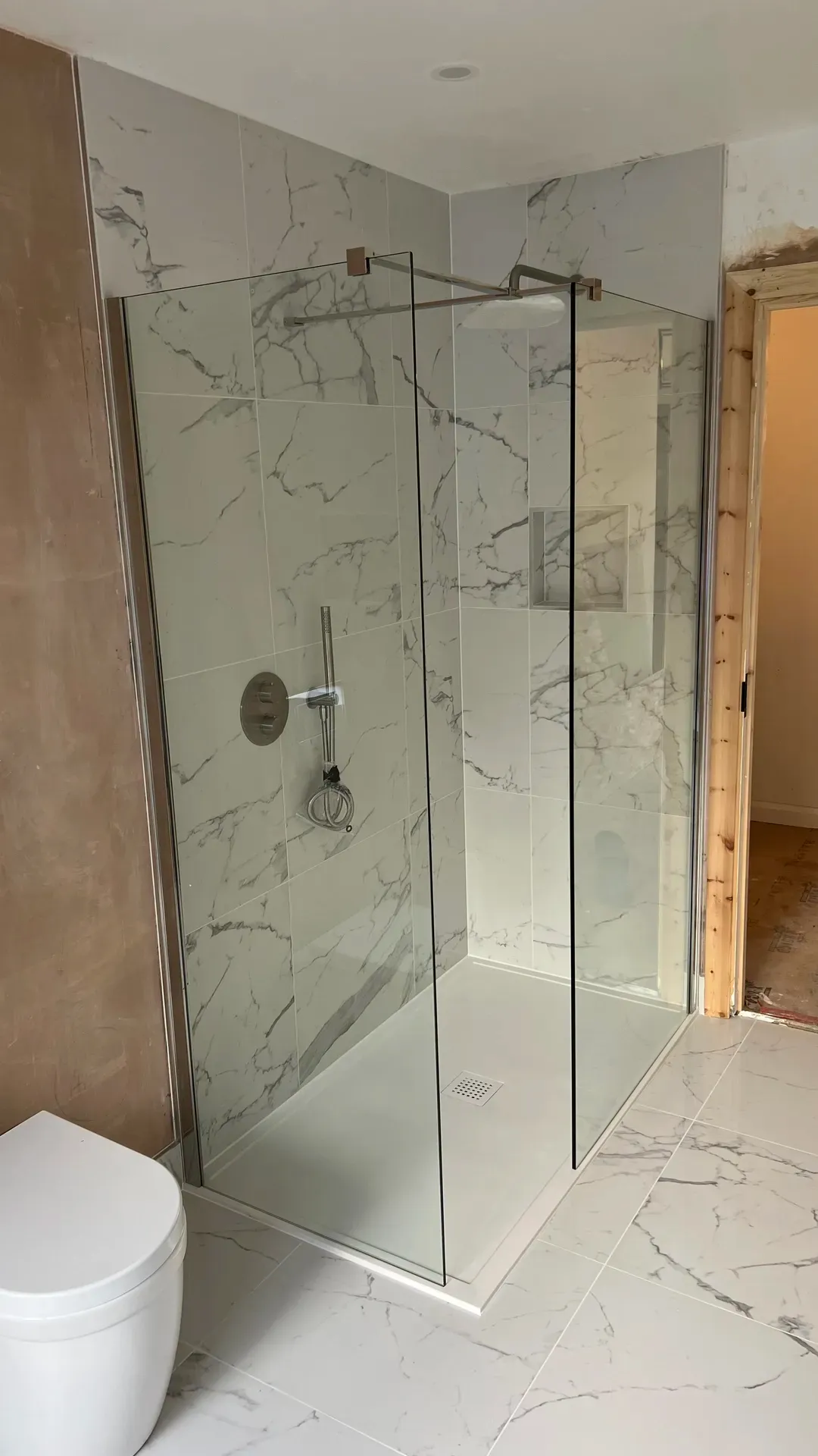 Frameless glass shower enclosure with a low-profile tray and marble-effect walls