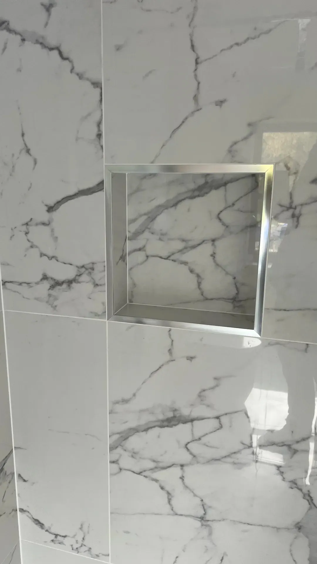Chrome-trimmed niche formed in a marble-effect tiled shower wall
