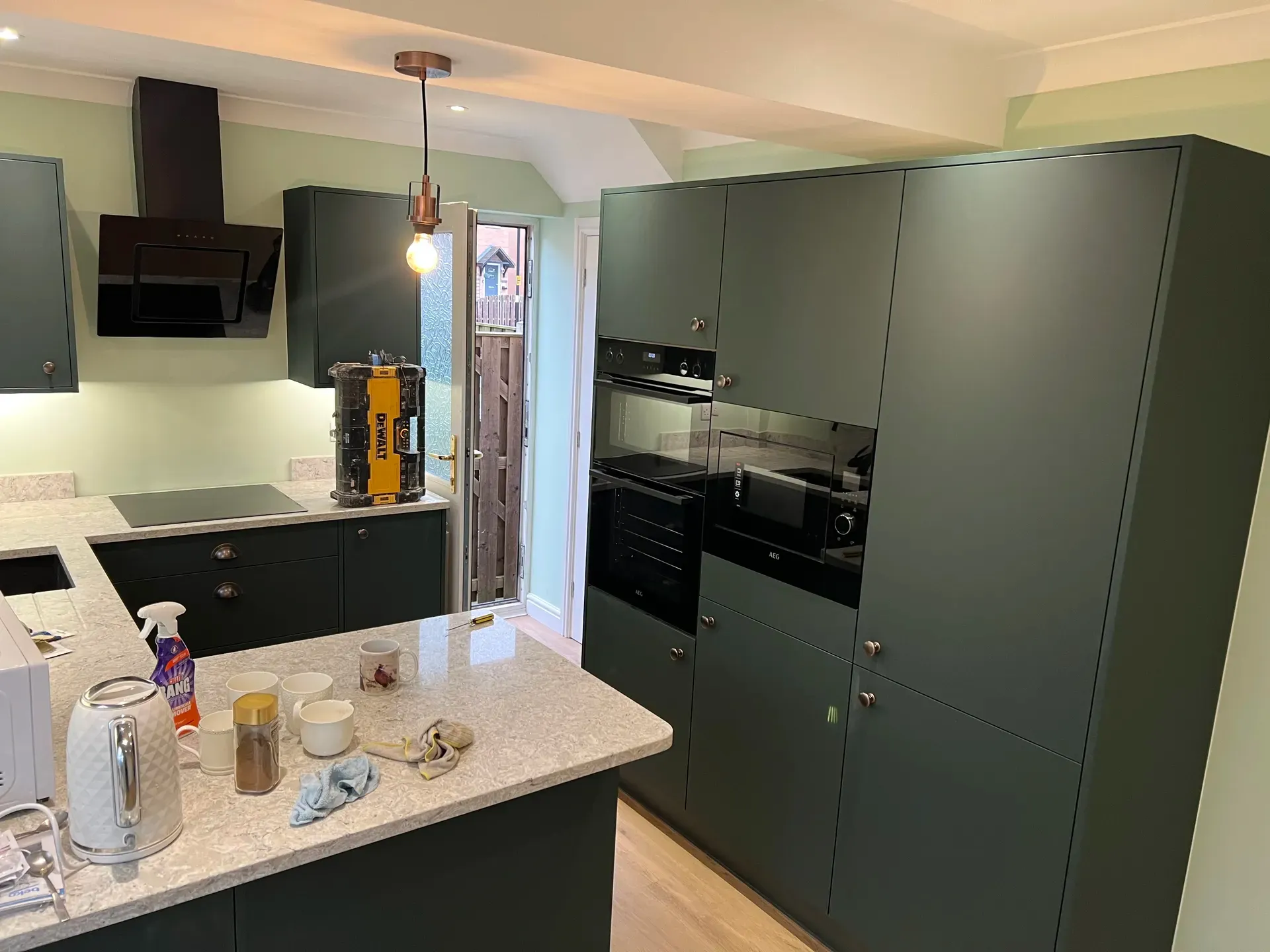 Dark green kitchen with an island, integrated appliances and pendant lights