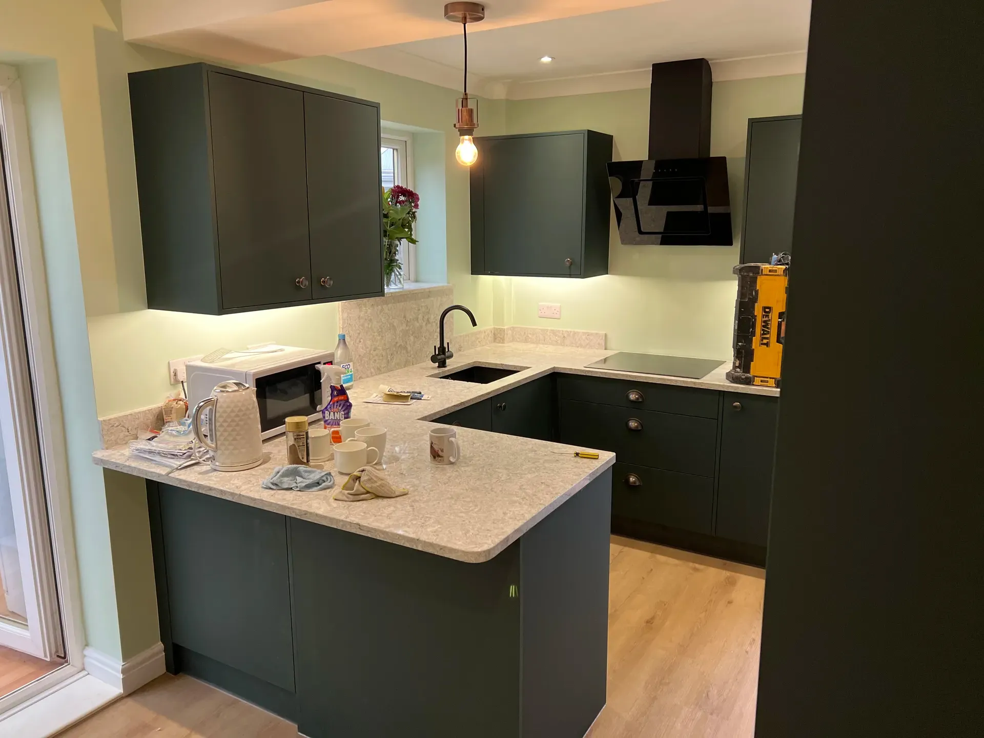 Dark green U-shaped kitchen with speckled worktops and pendant lighting