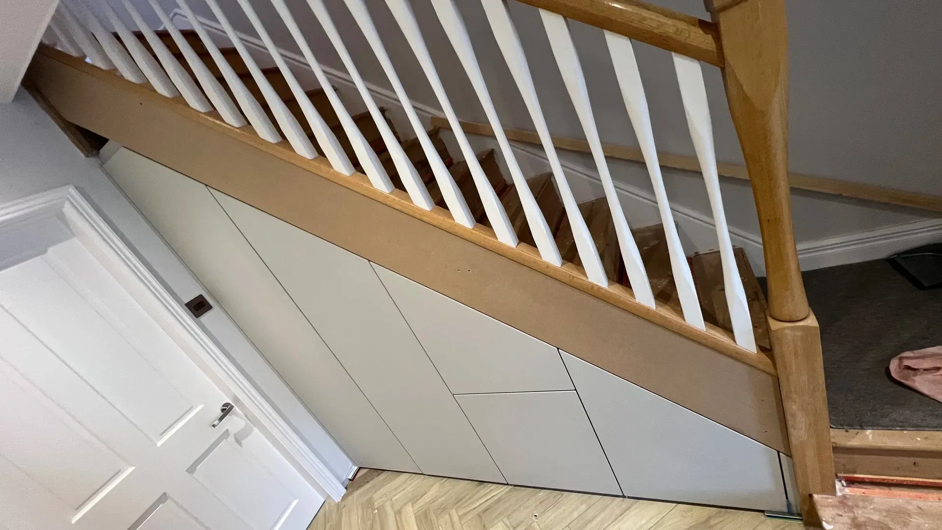 Fitted understairs storage with handleless doors beneath an open staircase