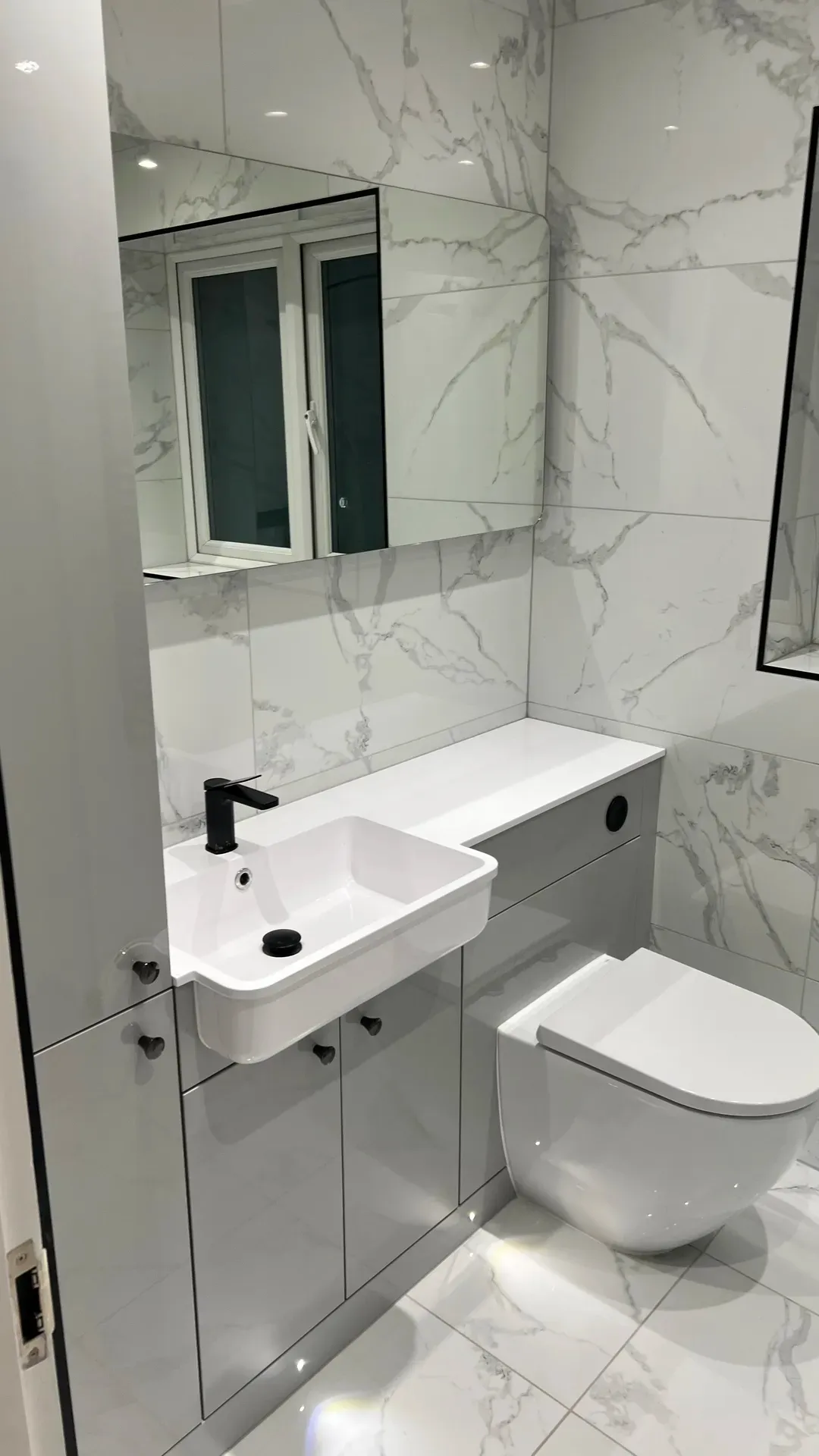 Wall-hung basin and toilet below a mirrored cabinet on marble-effect tiling