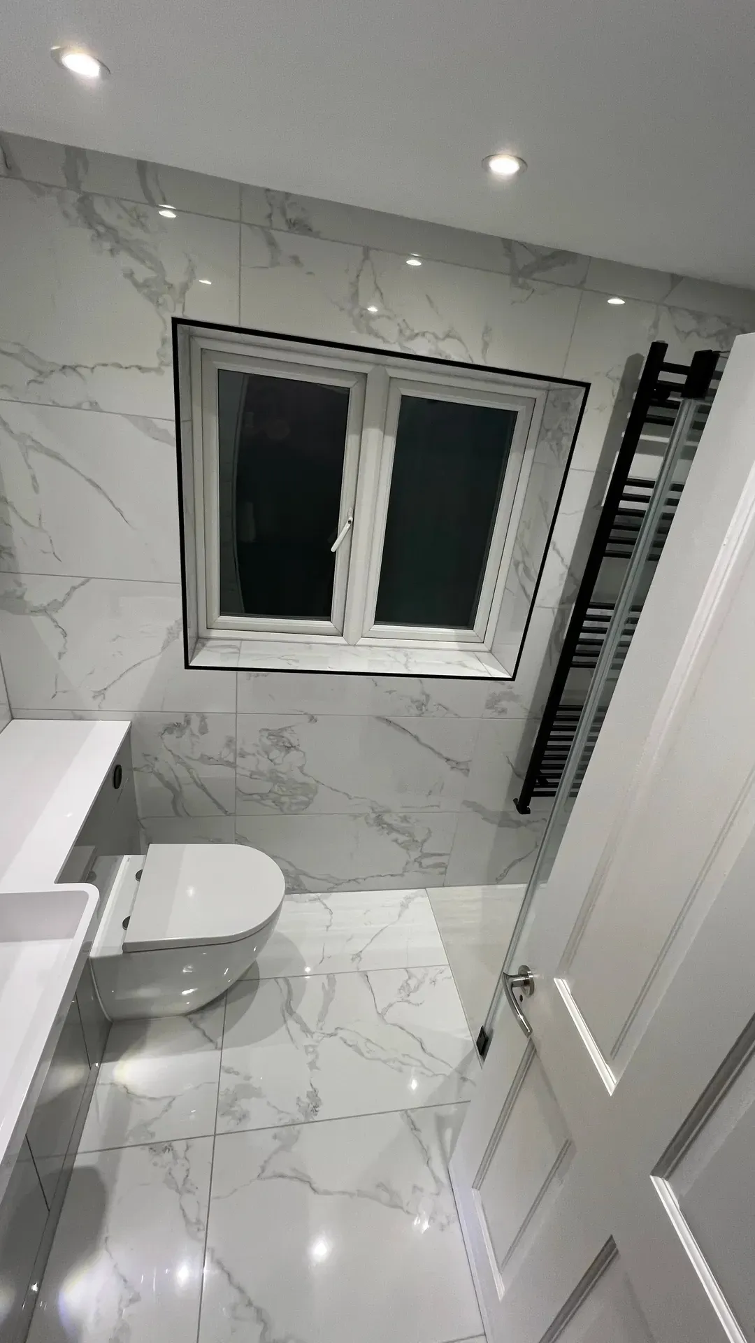 Basin and toilet beneath a window with a black ladder radiator alongside