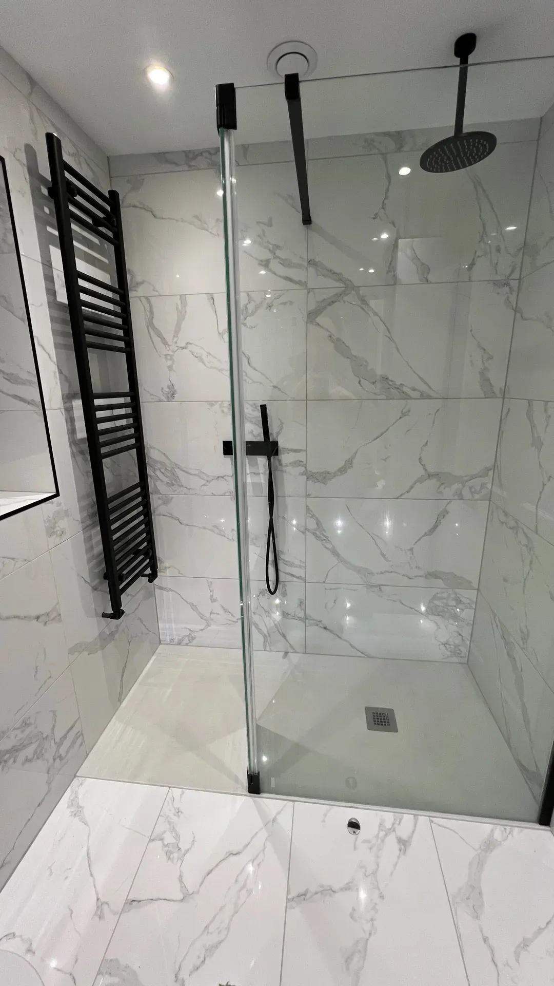 Walk-in shower with a black towel radiator and marble-effect wall tiles