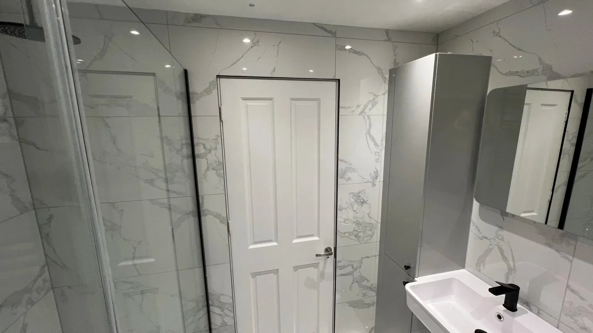Marble-effect tiling run around a panelled door in a shower room