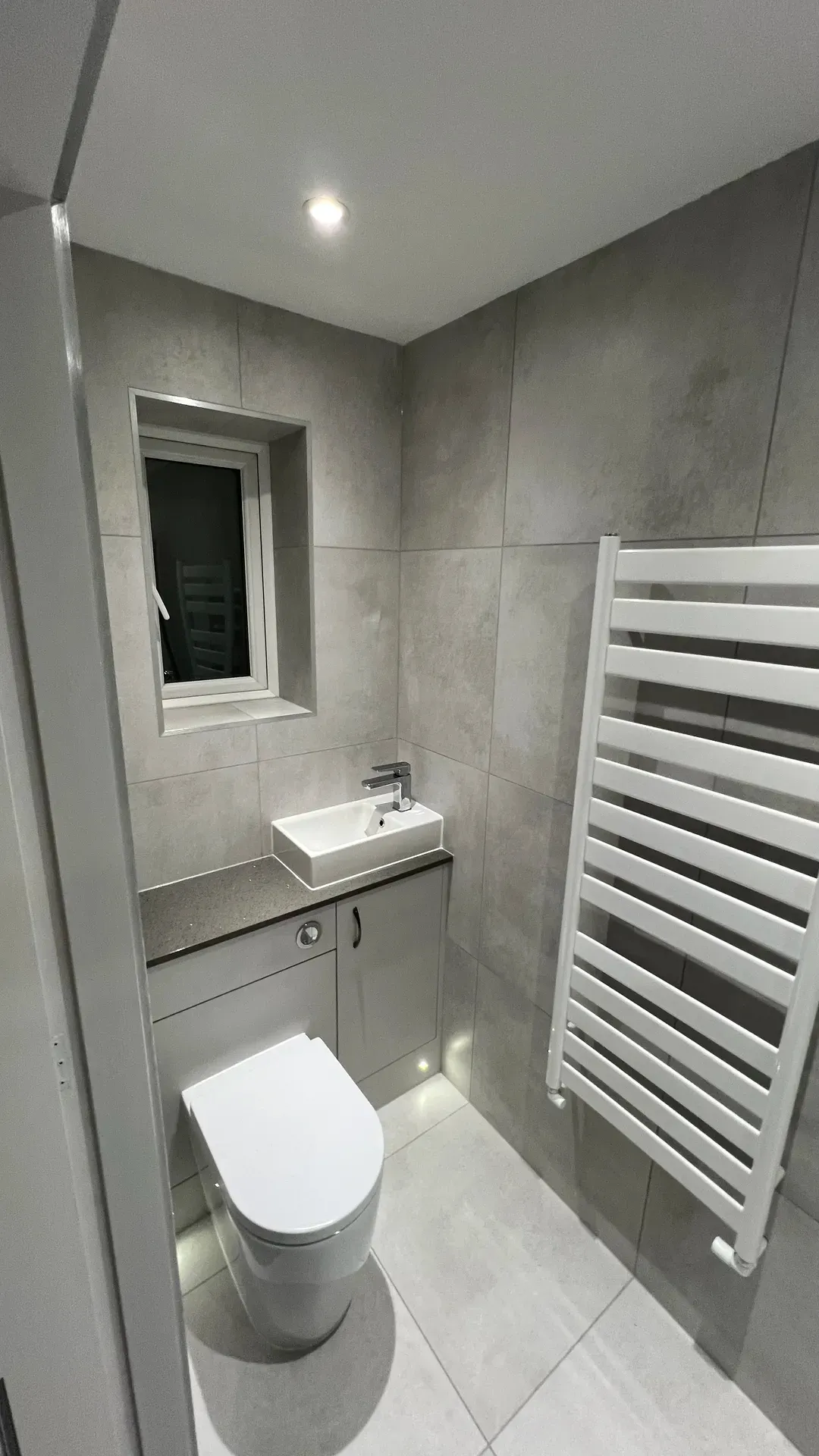 Vanity basin, toilet and white ladder radiator in a grey-tiled bathroom