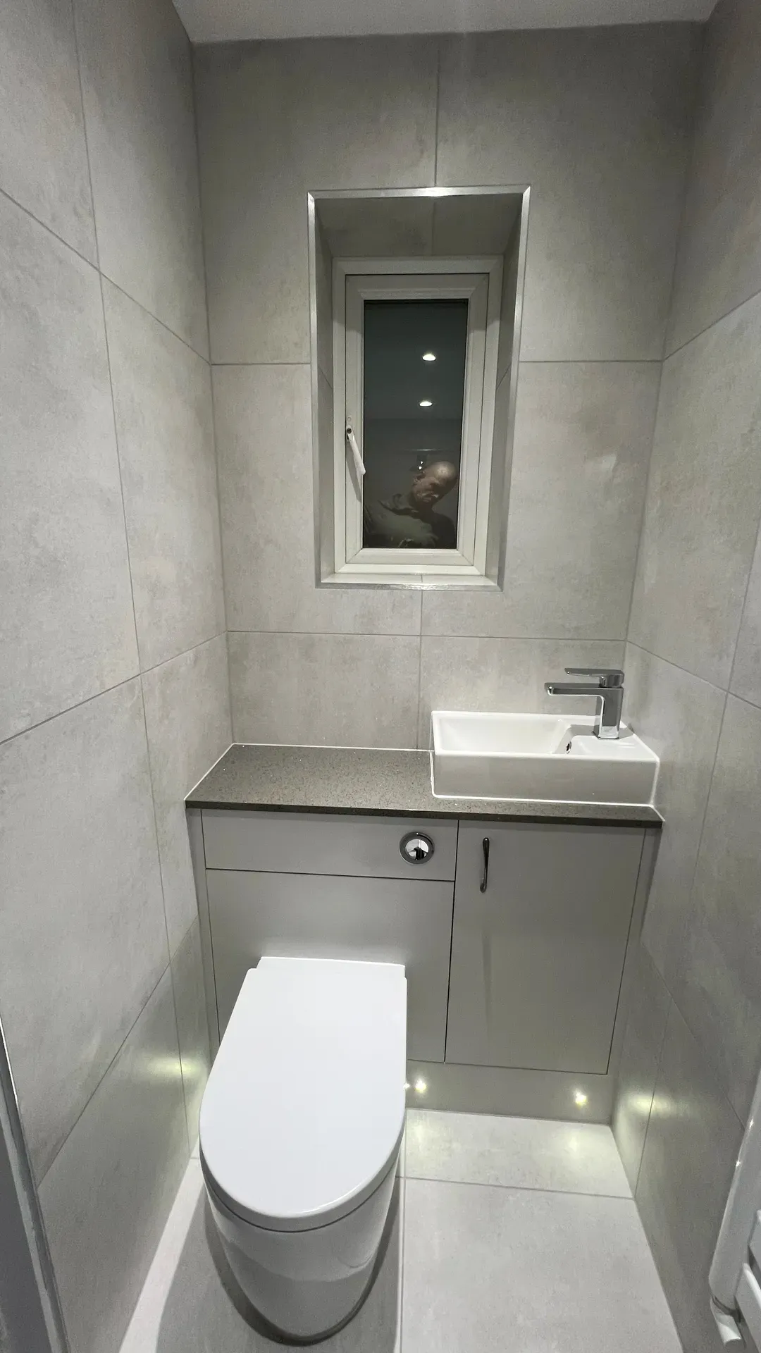 Vanity basin below a narrow window in a grey-tiled cloakroom
