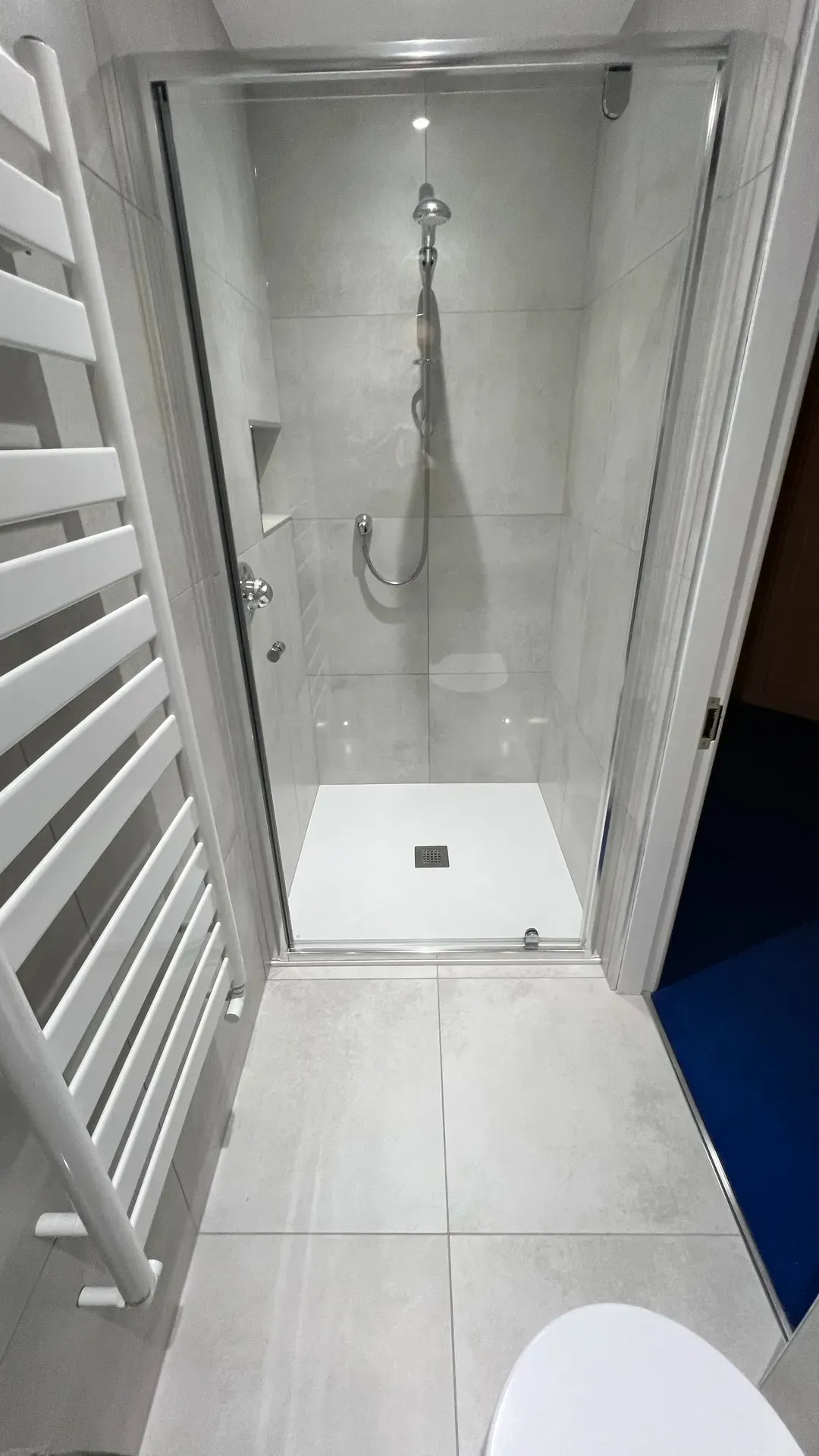 Low-profile shower tray and enclosure beside a white ladder radiator