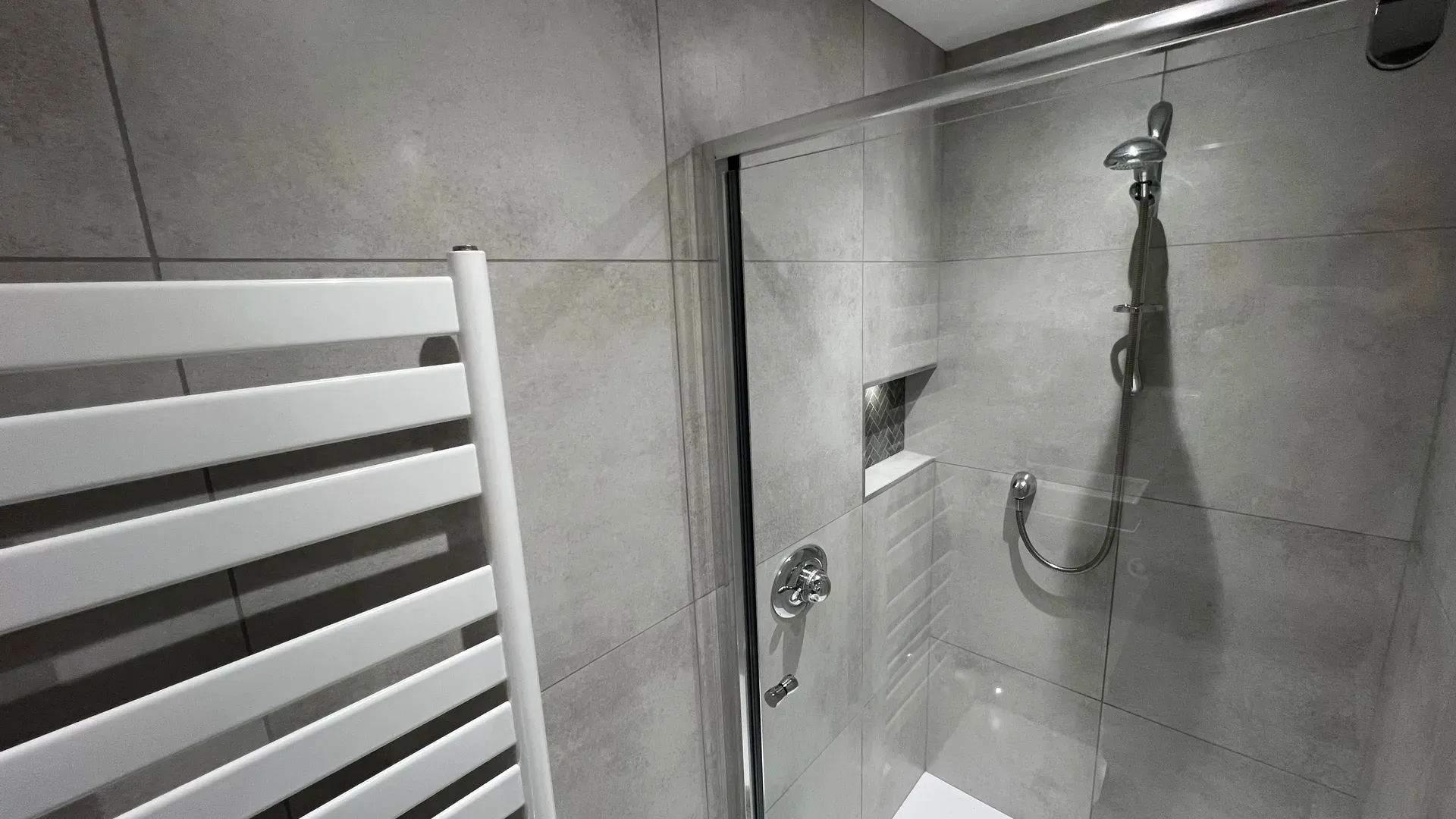 Walk-in shower with a recessed shelf, grab rail and white towel radiator
