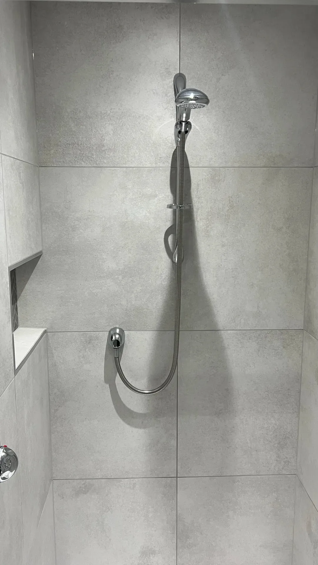 Grab rail, shower riser and recessed shelf on large-format grey tiling