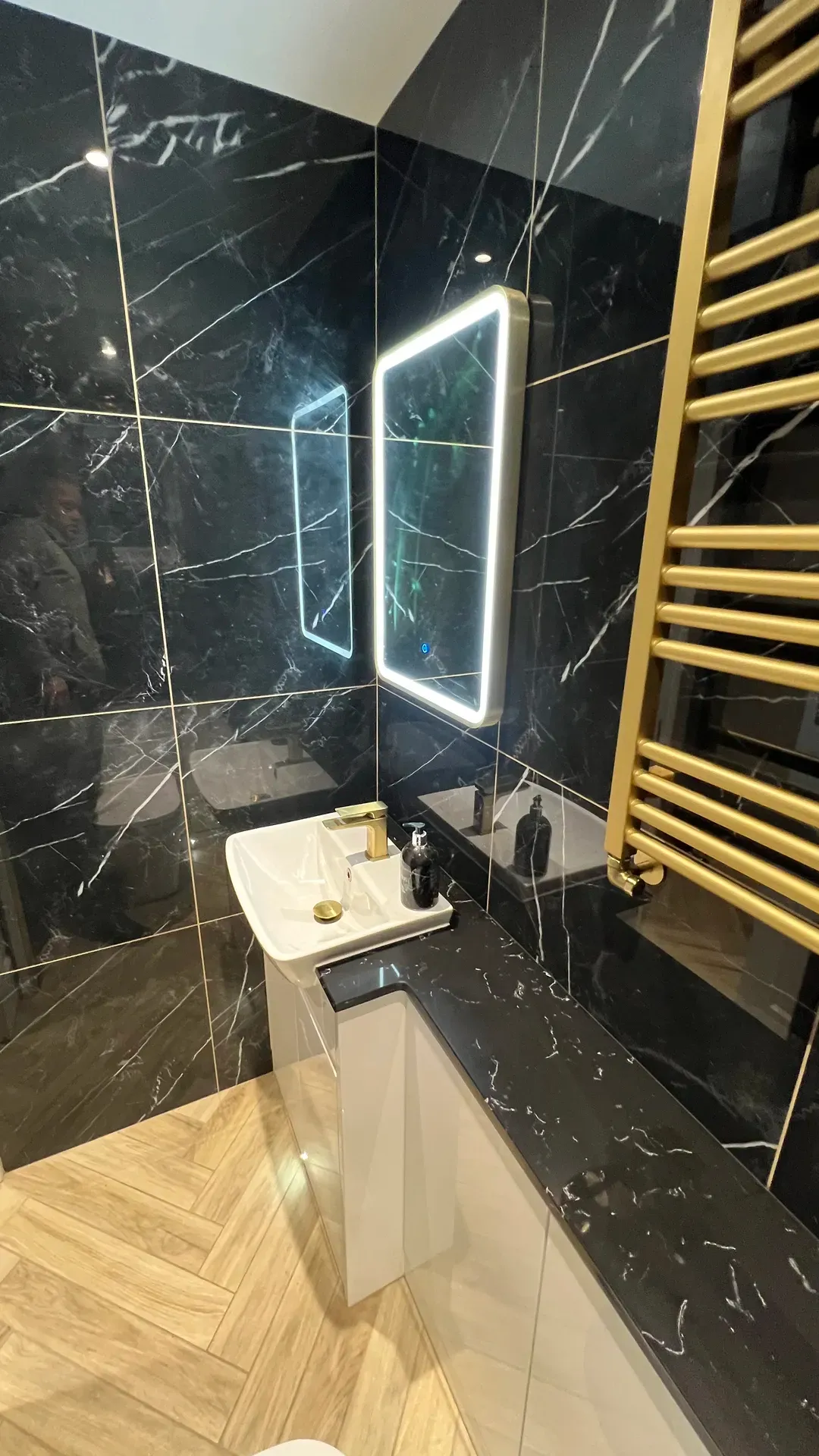 Black marble-effect cloakroom with a lit mirror and a brass towel radiator