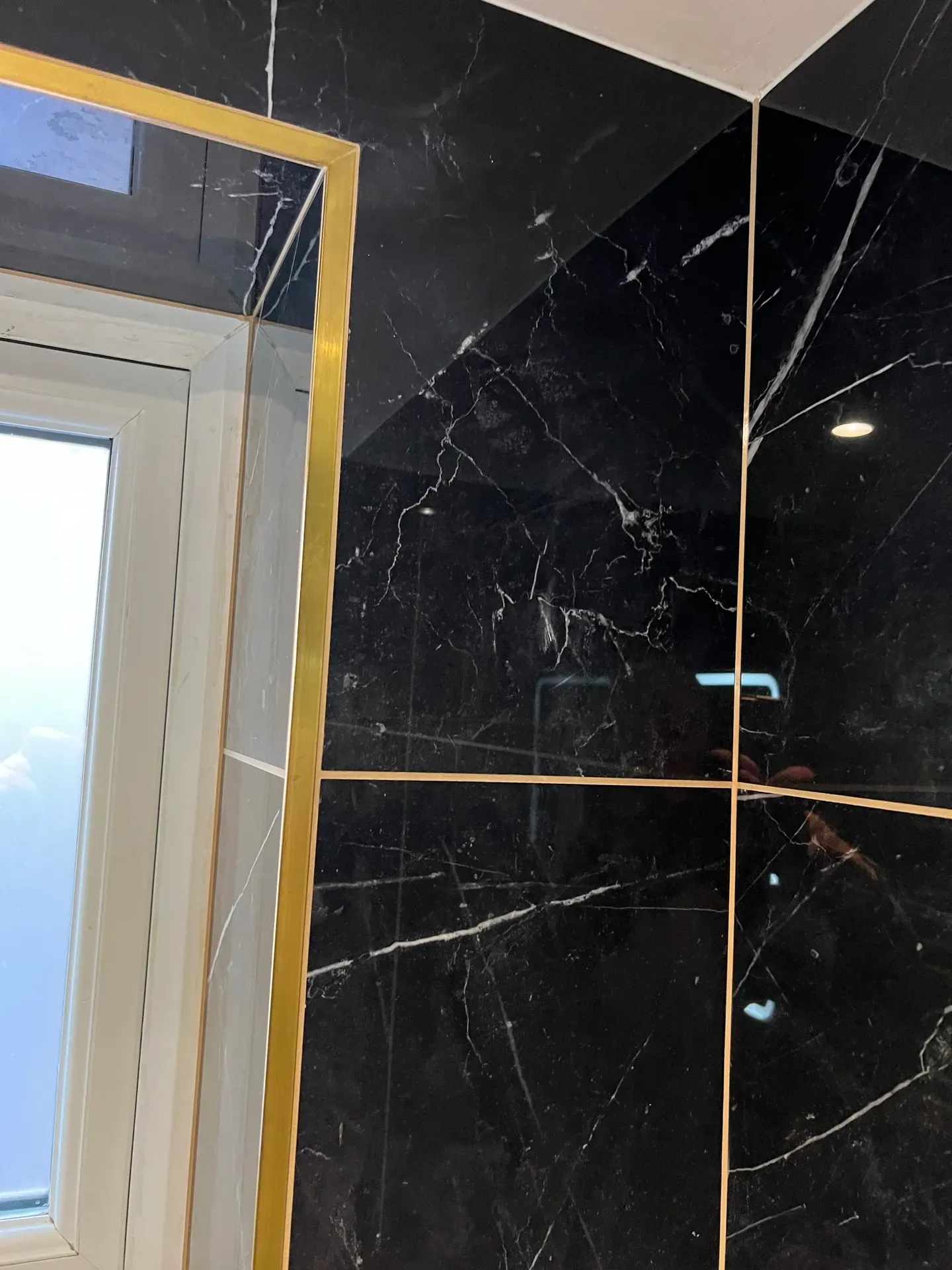 Black marble-effect wall tiling with brass inlay trim beside a window