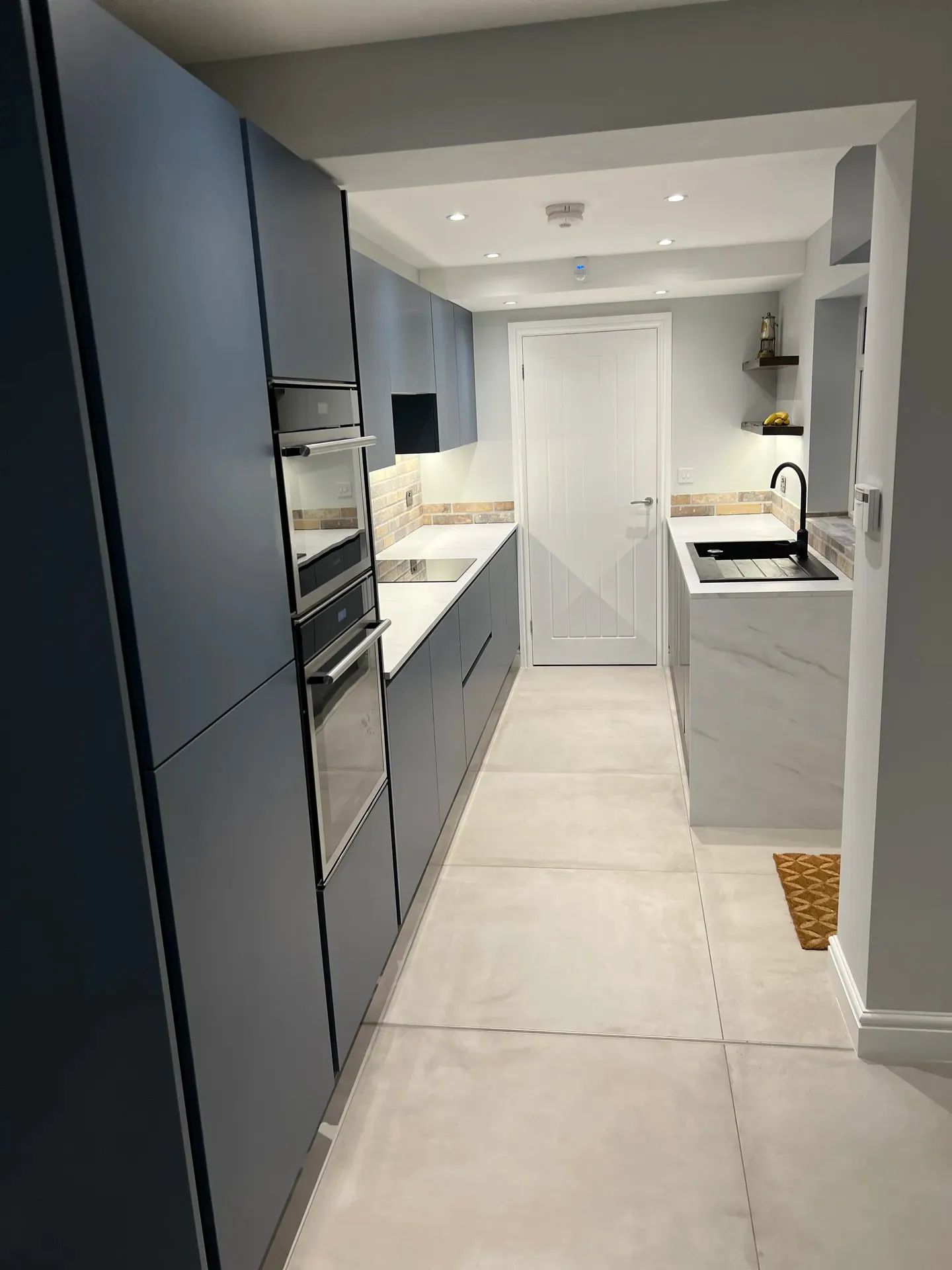 Handleless dark blue kitchen with an island, white worktops and a tiled floor