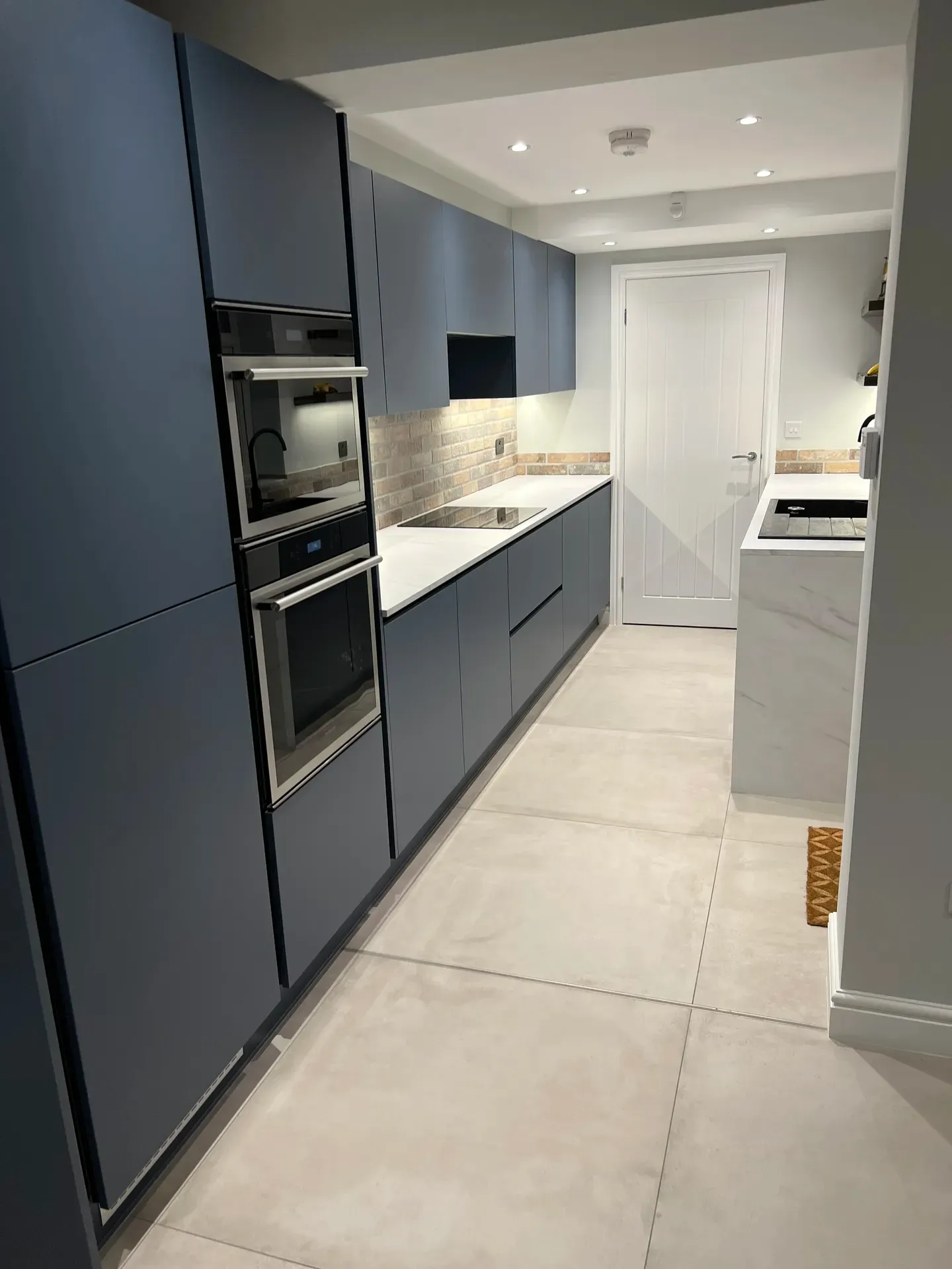 Dark blue handleless kitchen with built-in ovens and under-cabinet lighting