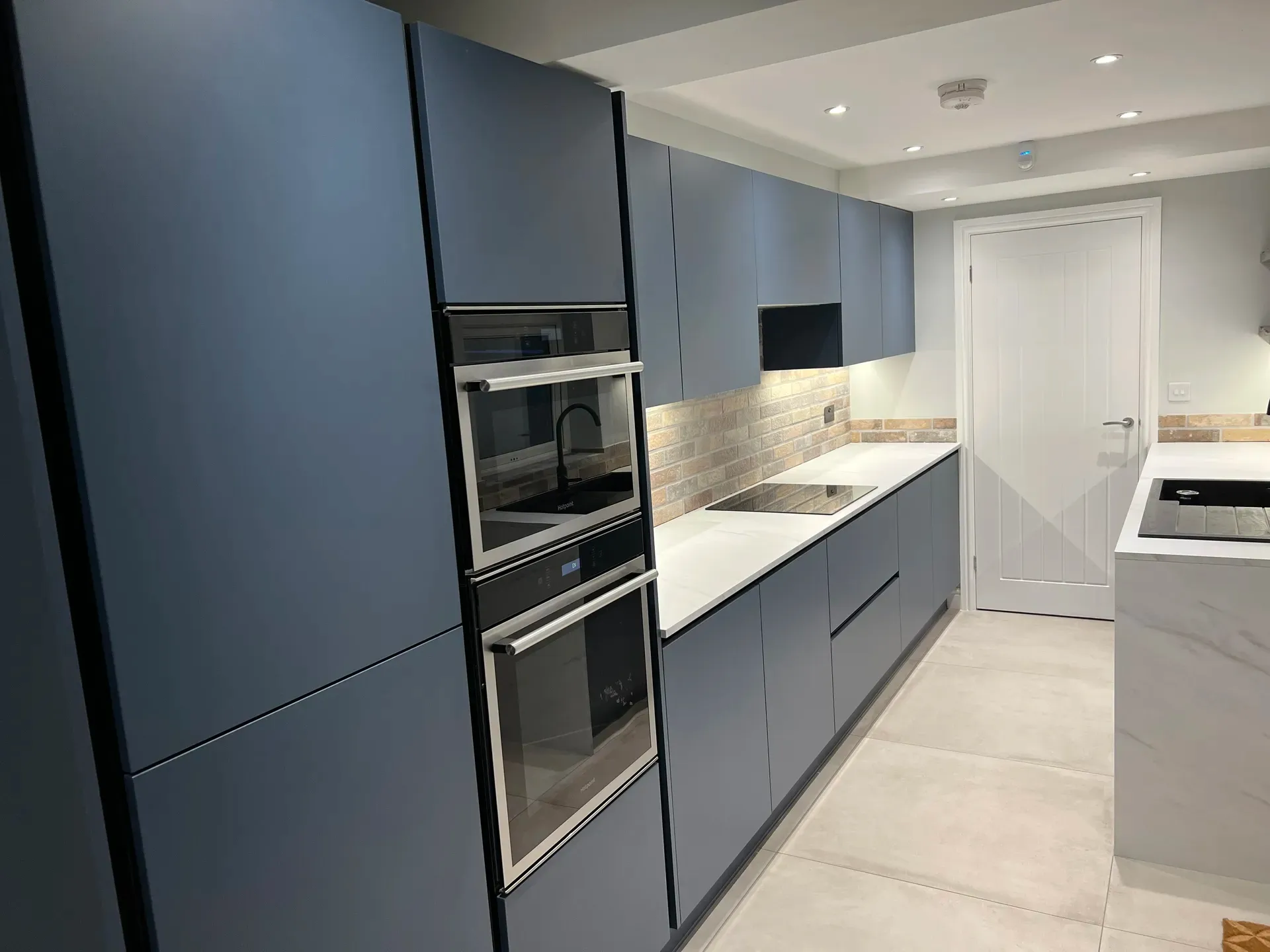 Built-in double oven and induction hob in a handleless dark blue kitchen