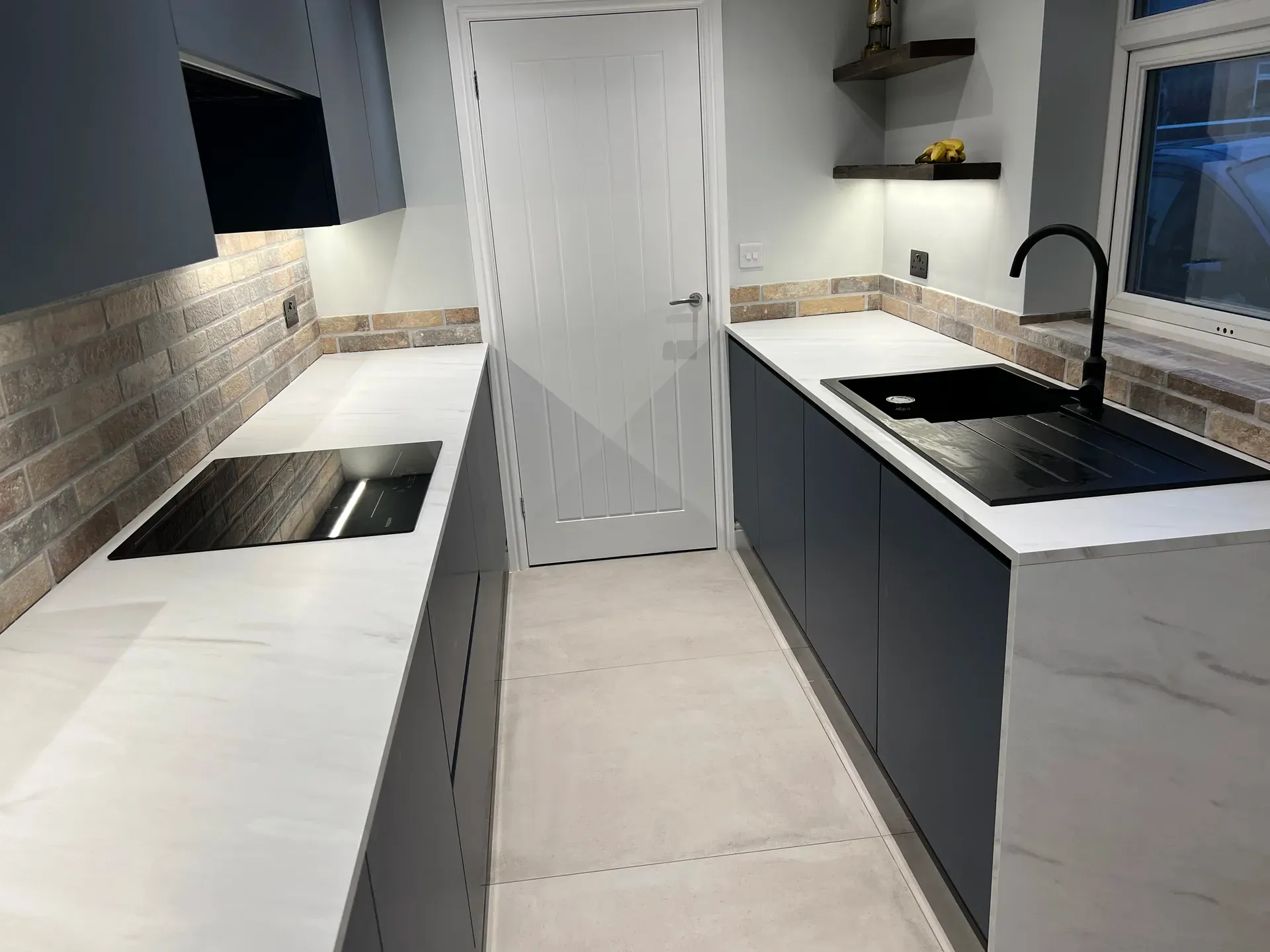 Galley kitchen with a black sink, induction hob and brick-effect splashback