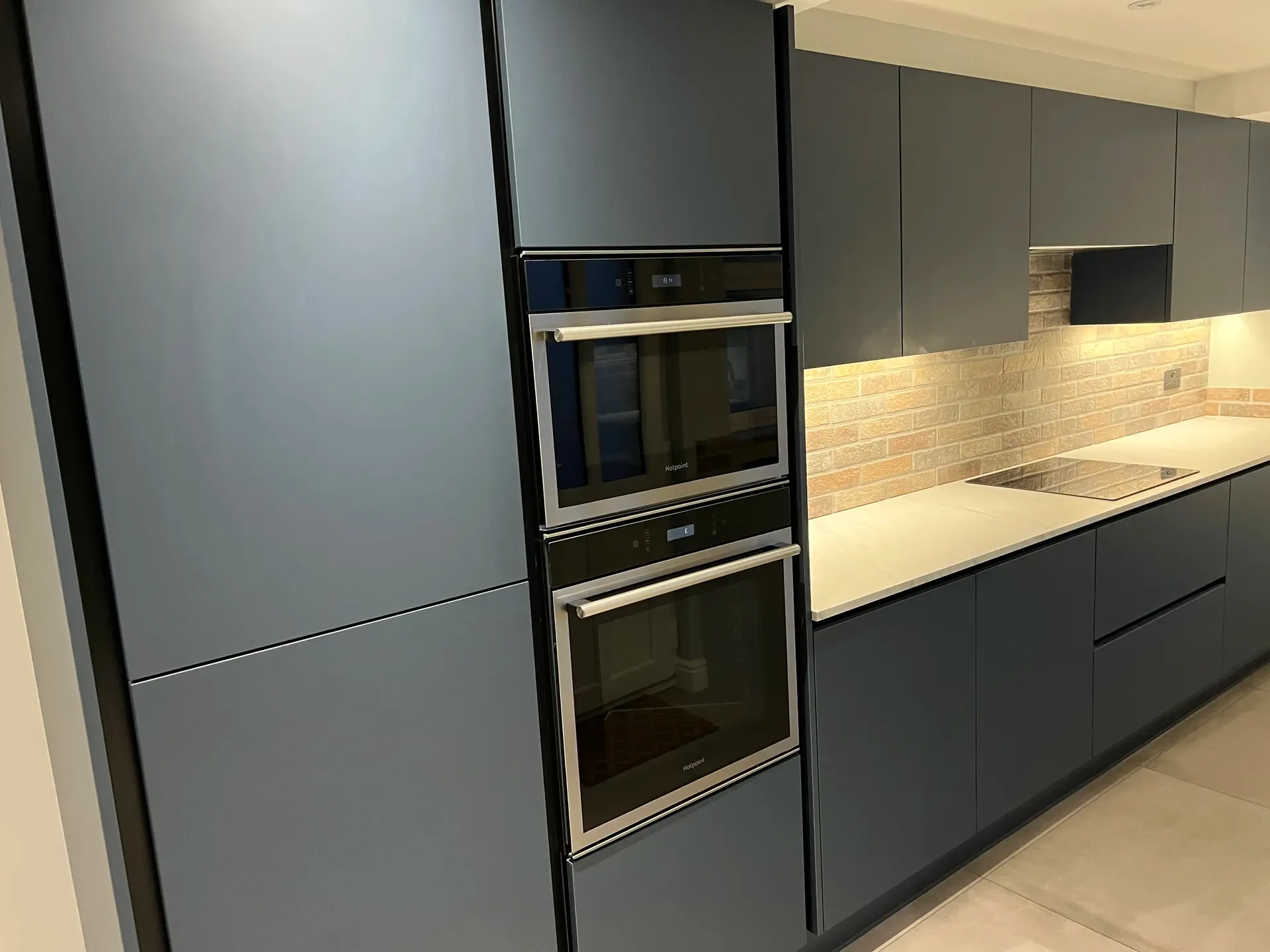 Tall oven housing and lit worktop in a handleless dark blue kitchen