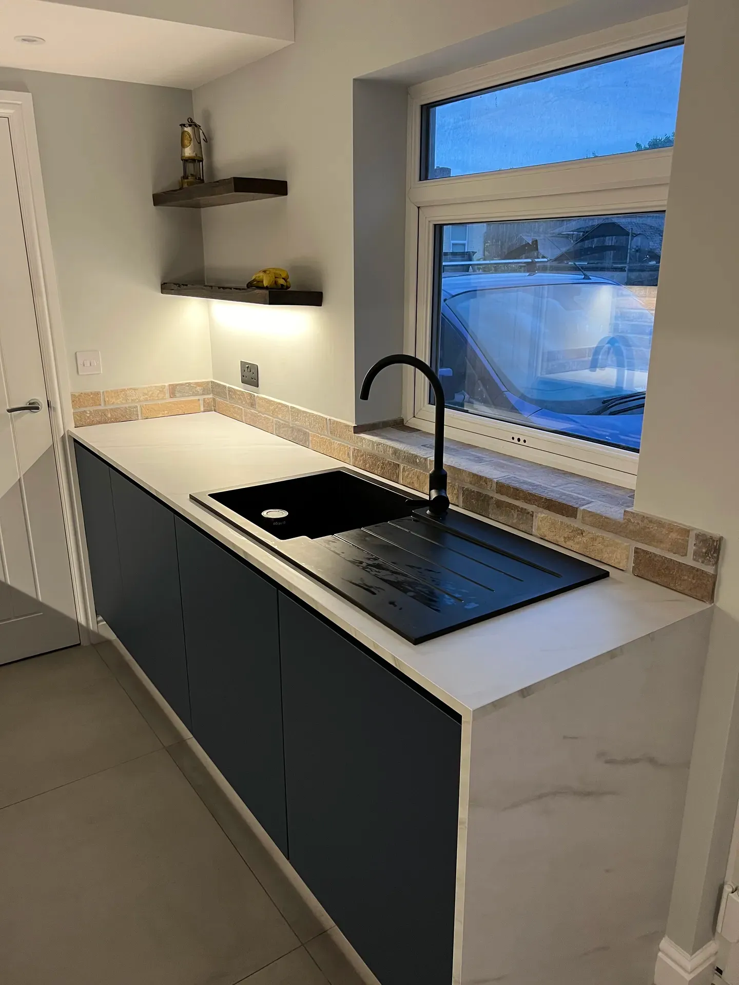 Black composite sink and induction hob under a window with a brick splashback