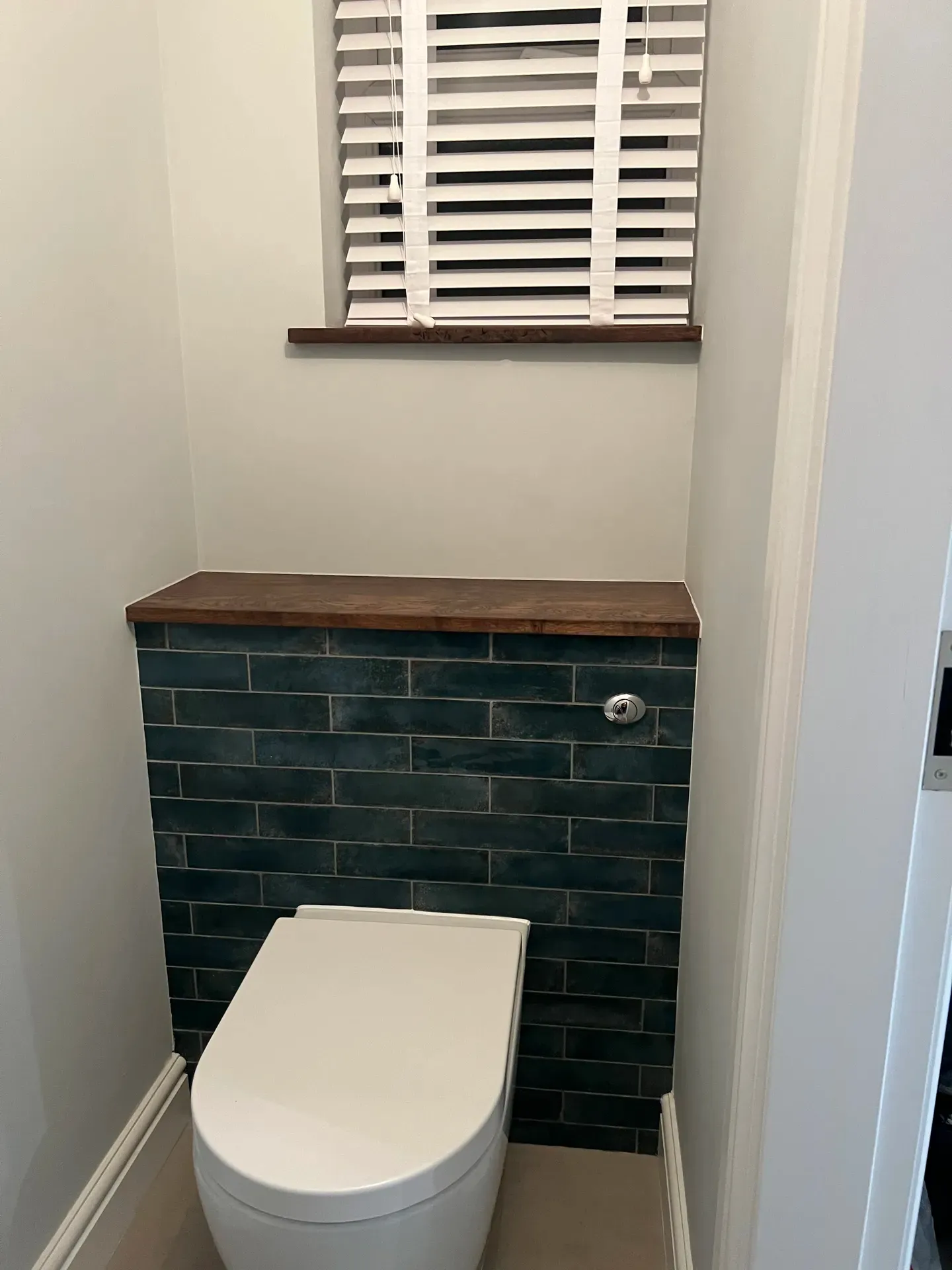 Toilet set into a green metro-tiled boxing with a solid timber shelf